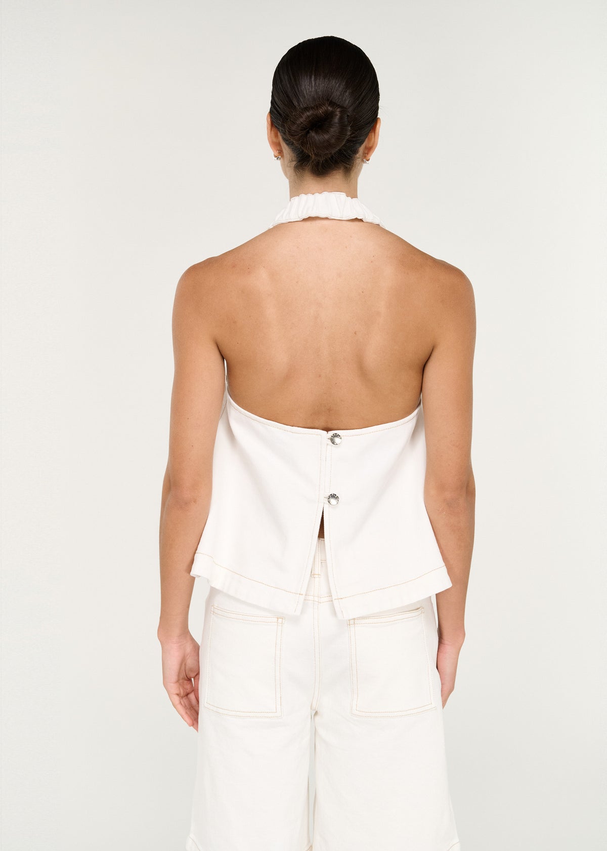 Back view of the Cotton Denim Halter Top in White with an open back and a branded button closure at back.