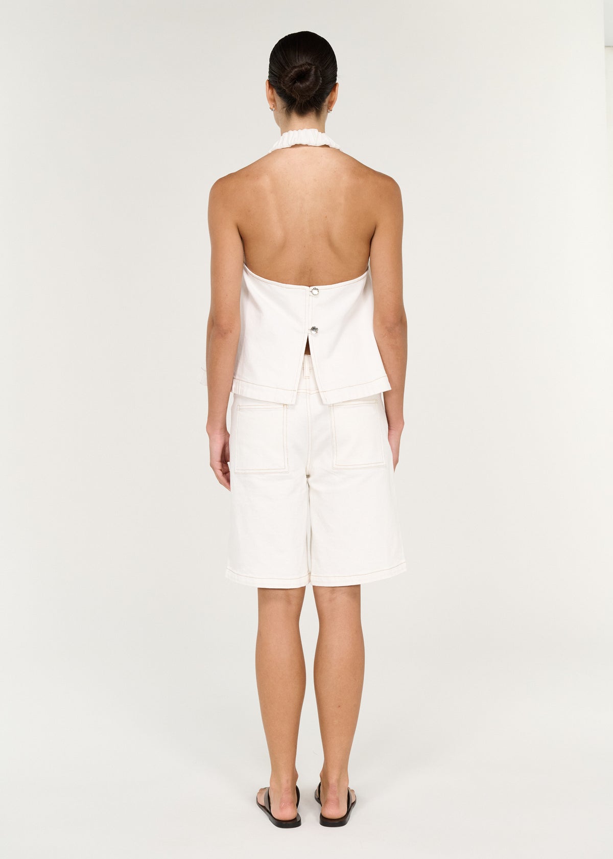 Back view of the Cotton Denim Halter Top in White, showing an open back and a branded button closure at back.