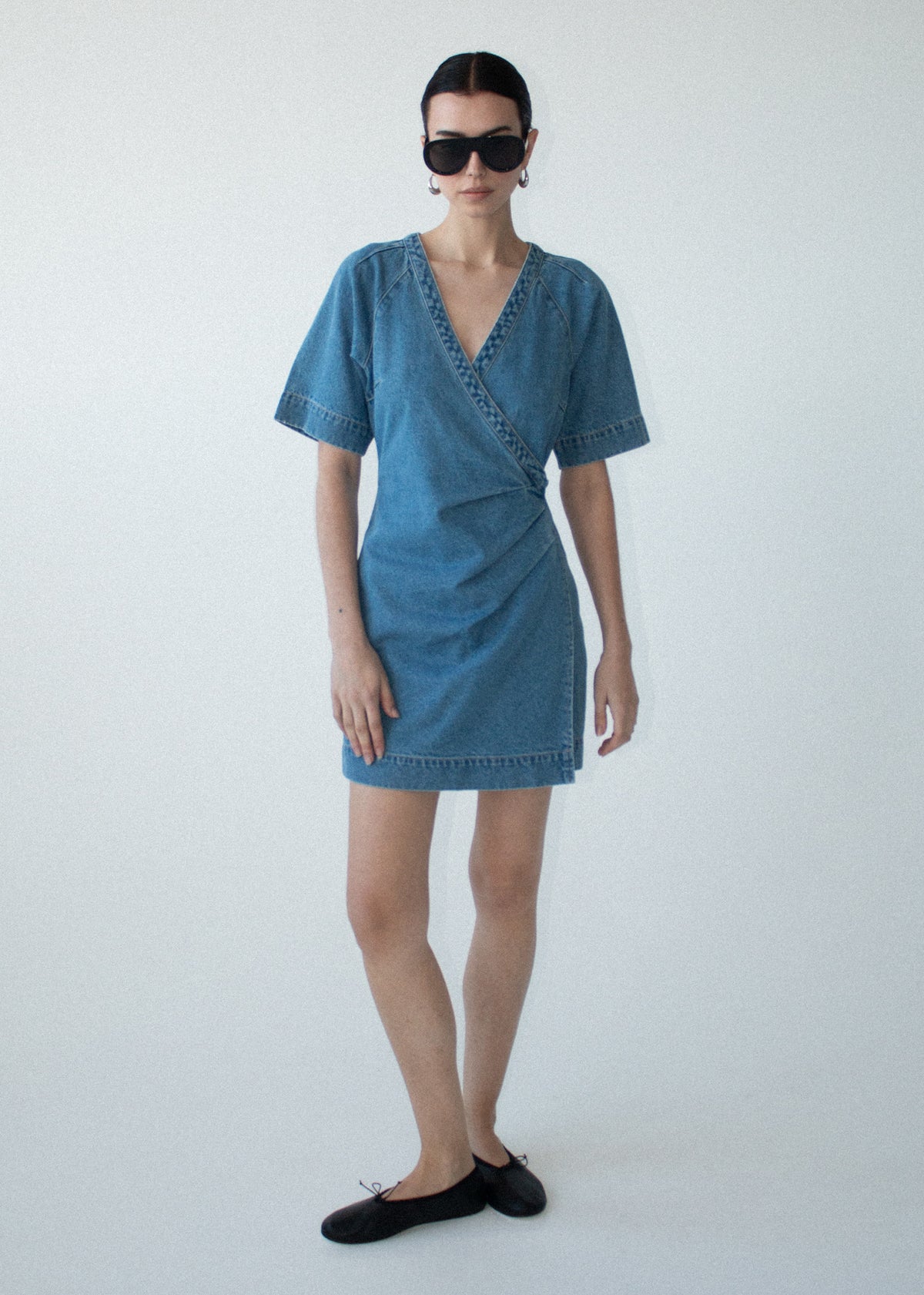 Model wearing Cotton Denim Wrap Detail Mini Dress with a mini length silhouette and a deep V-neckline.