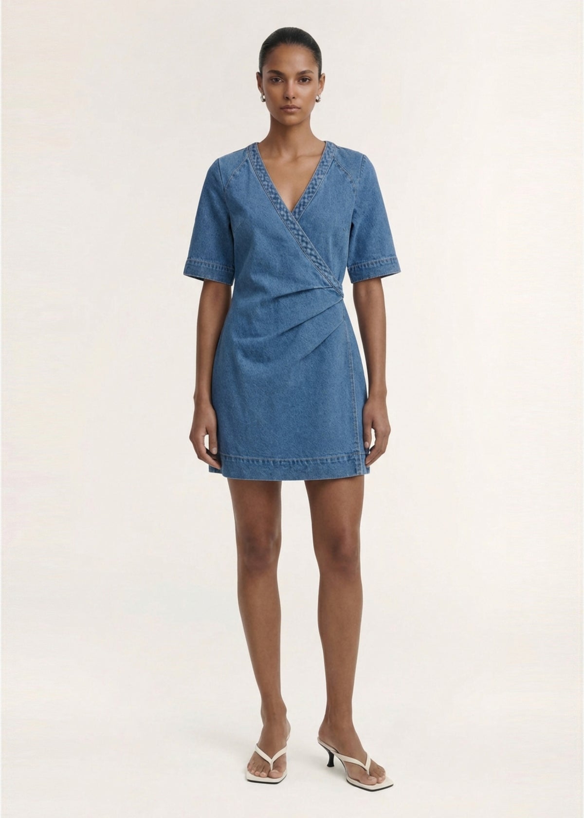 Model wearing Cotton Denim Wrap Detail Mini Dress, showing a designed and a soft mid-wash denim fabrication.
