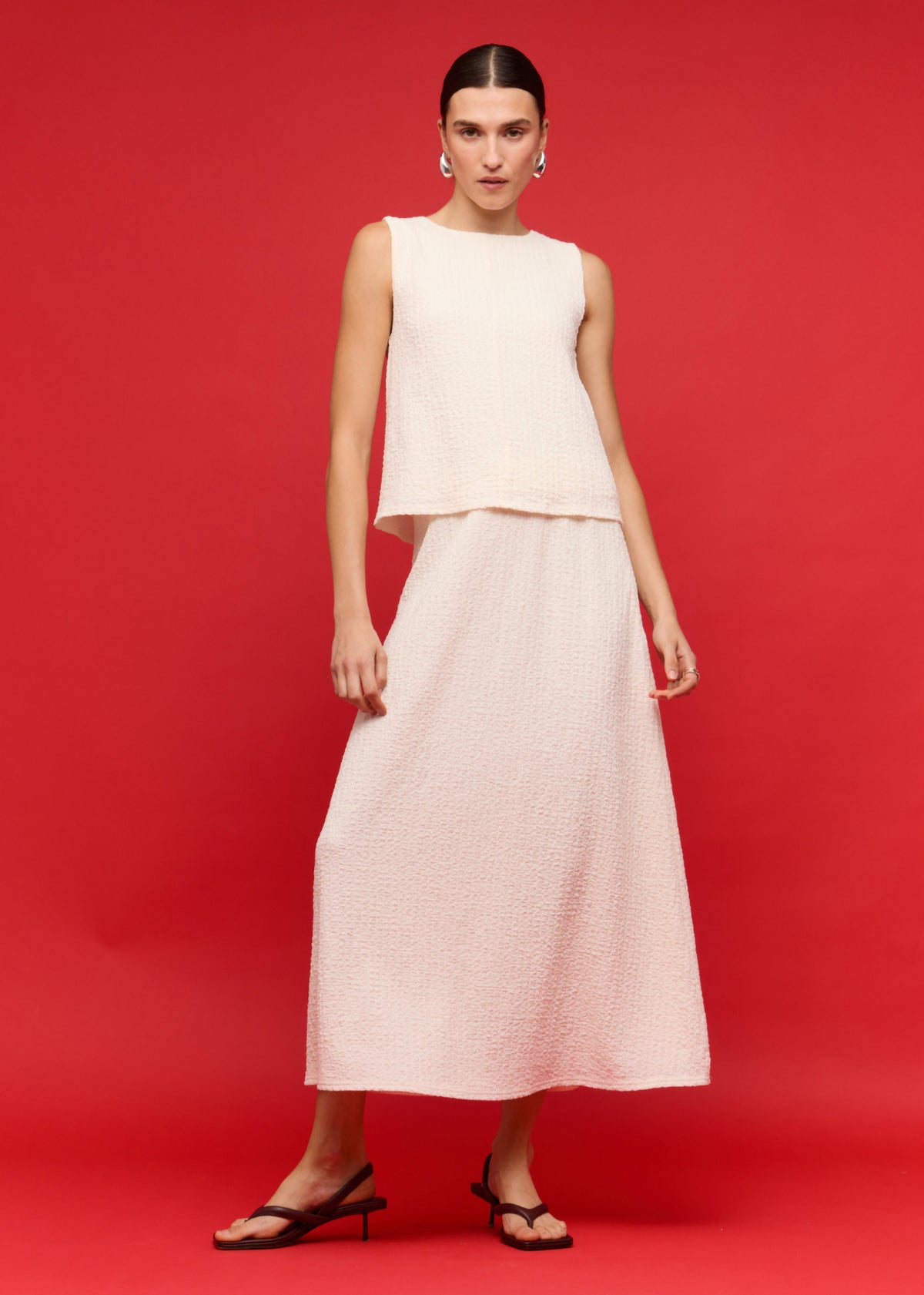 Model wearing Cream A-Line Midi Skirt, showing a midi length, photographed against a red studio backdrop.