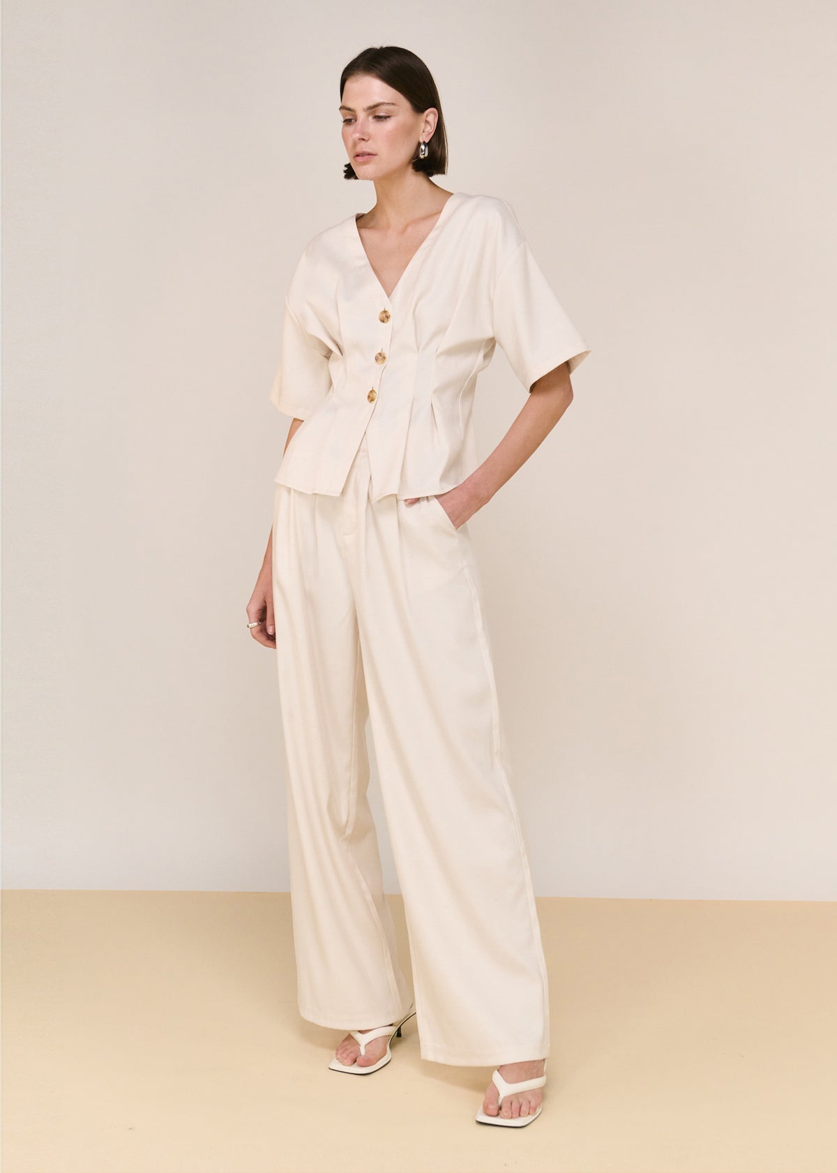 Model wearing Cream High Waisted Drape Pant with a high-waisted fit and a relaxed wide-leg silhouette.
