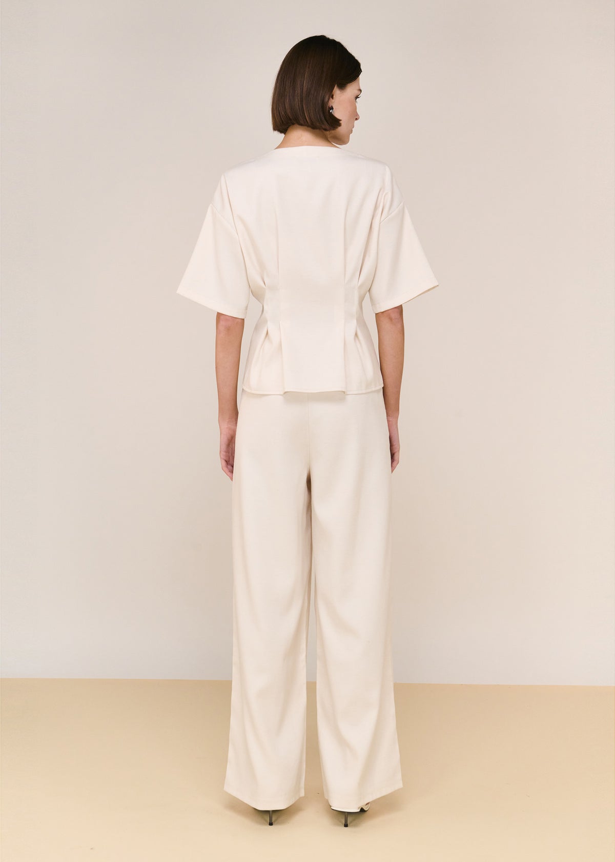 Back view of the Cream High Waisted Drape Pant with a high-waisted fit and a relaxed wide-leg silhouette.