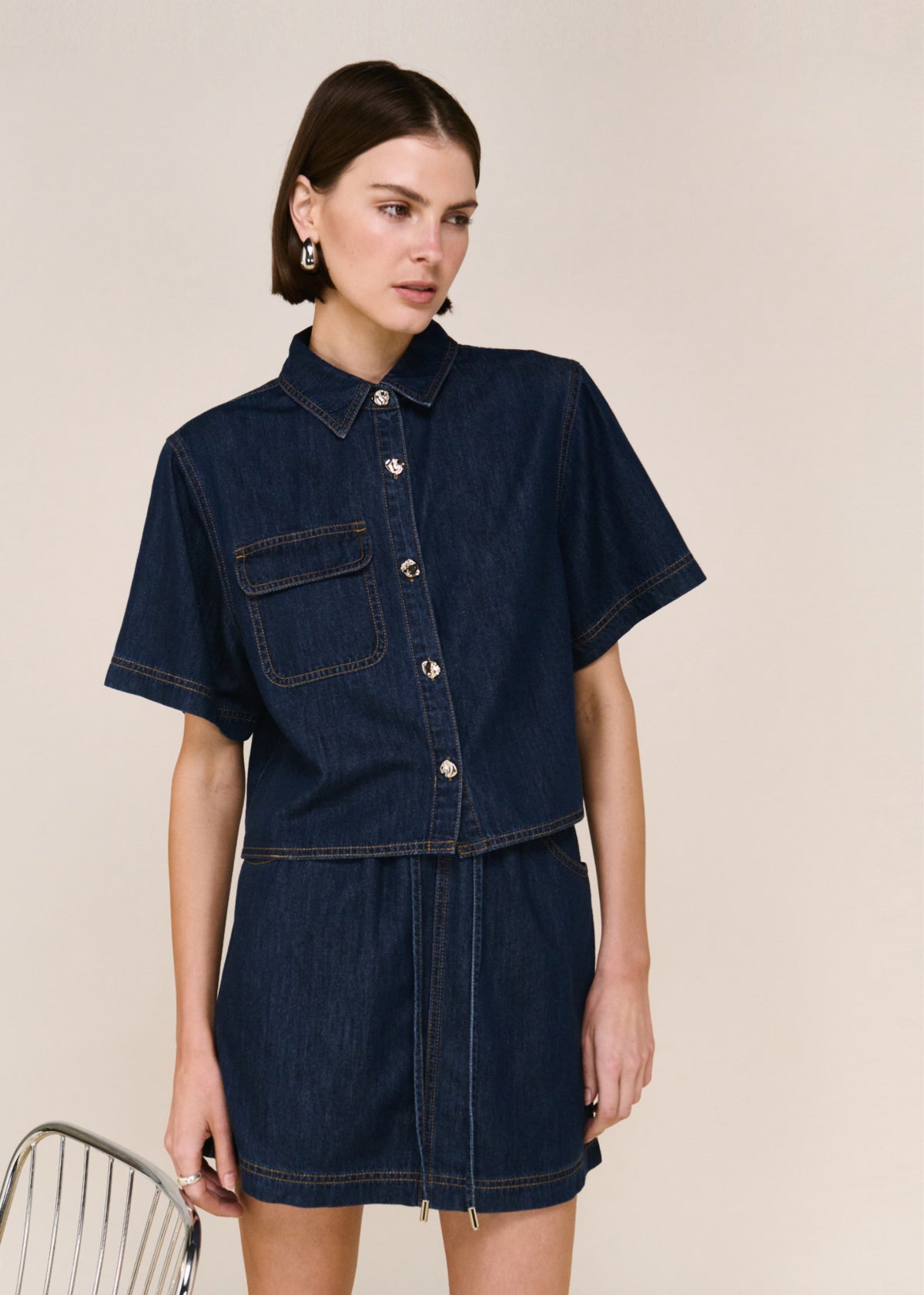 Model wearing Denim Elasticated Mini Skirt with an elasticated waistband and a contrast topstitch detailing, turned to the side.