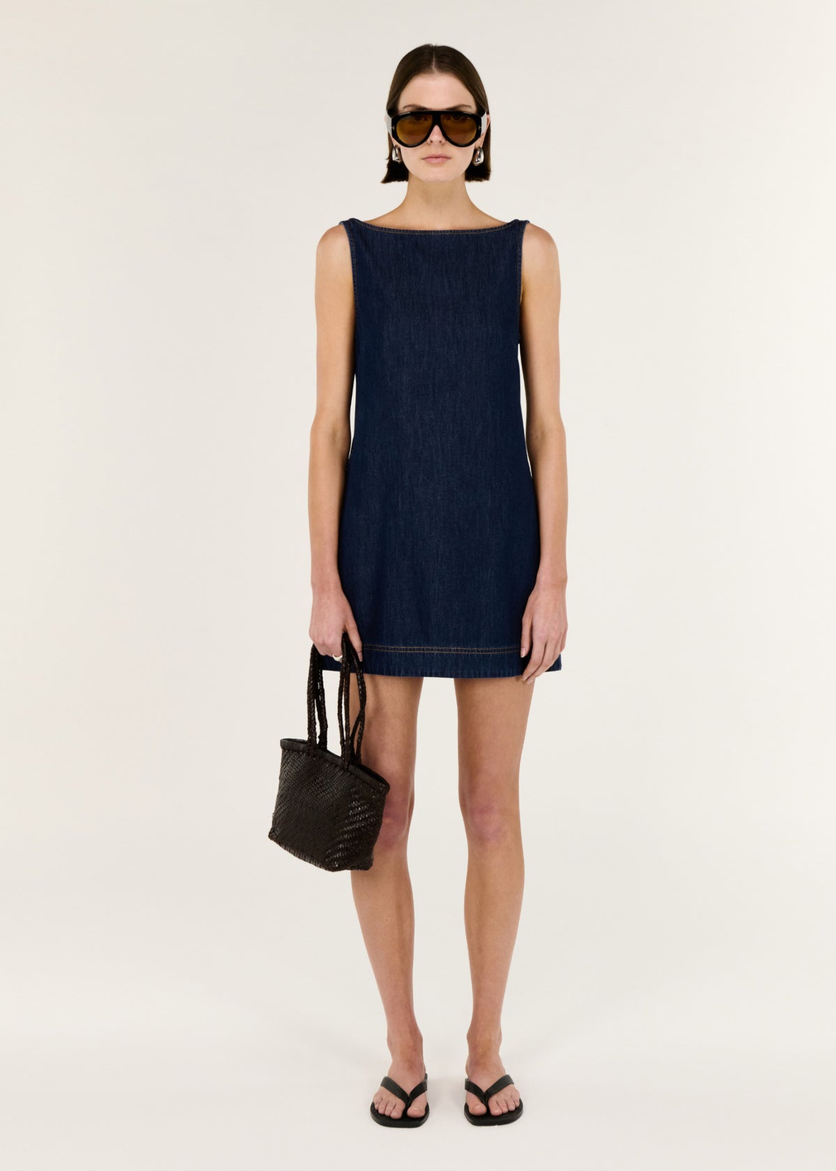 Model wearing Denim Mini Dress with Scoop Back with a sleeveless denim mini dress Clean A-line silhouette and a scoop back neckline.