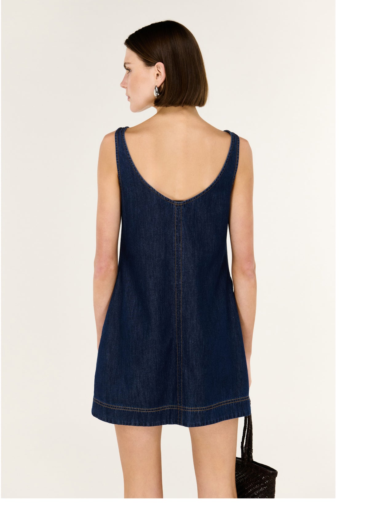 Back view of the Denim Mini Dress with Scoop Back with a scoop back neckline and a sleeveless denim mini dress Clean A-line silhouette.