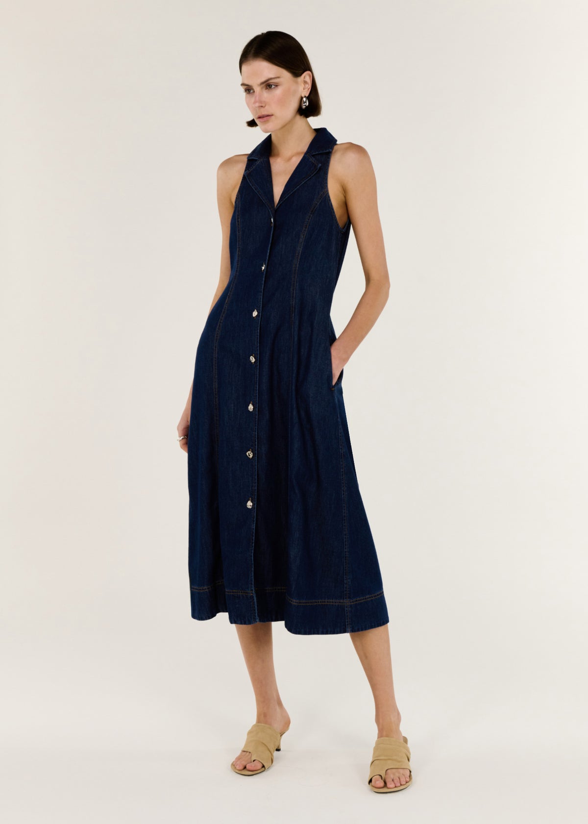 Angled view of the Denim Sleeveless Midi Shirt Dress with a button-through front and a midi length.