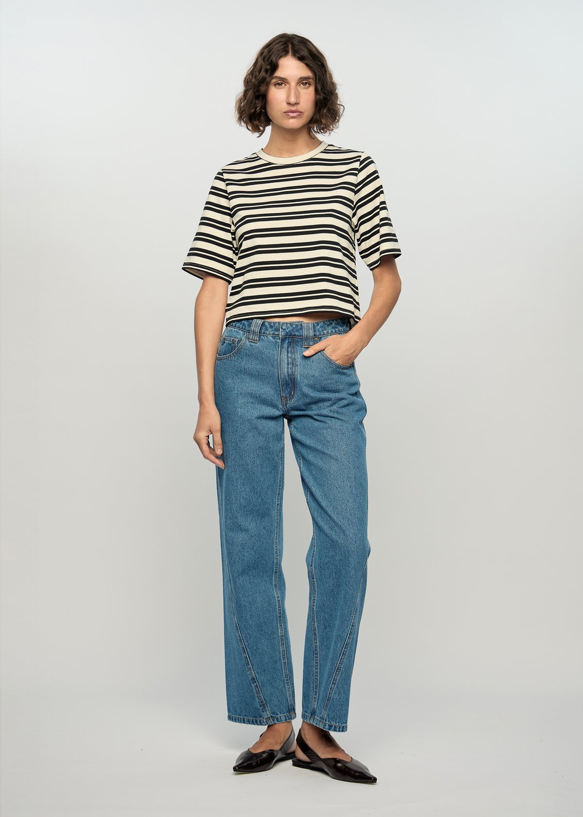 Model wearing Elara Crop Tee with a black and ivory stripe pattern, turned to the side.