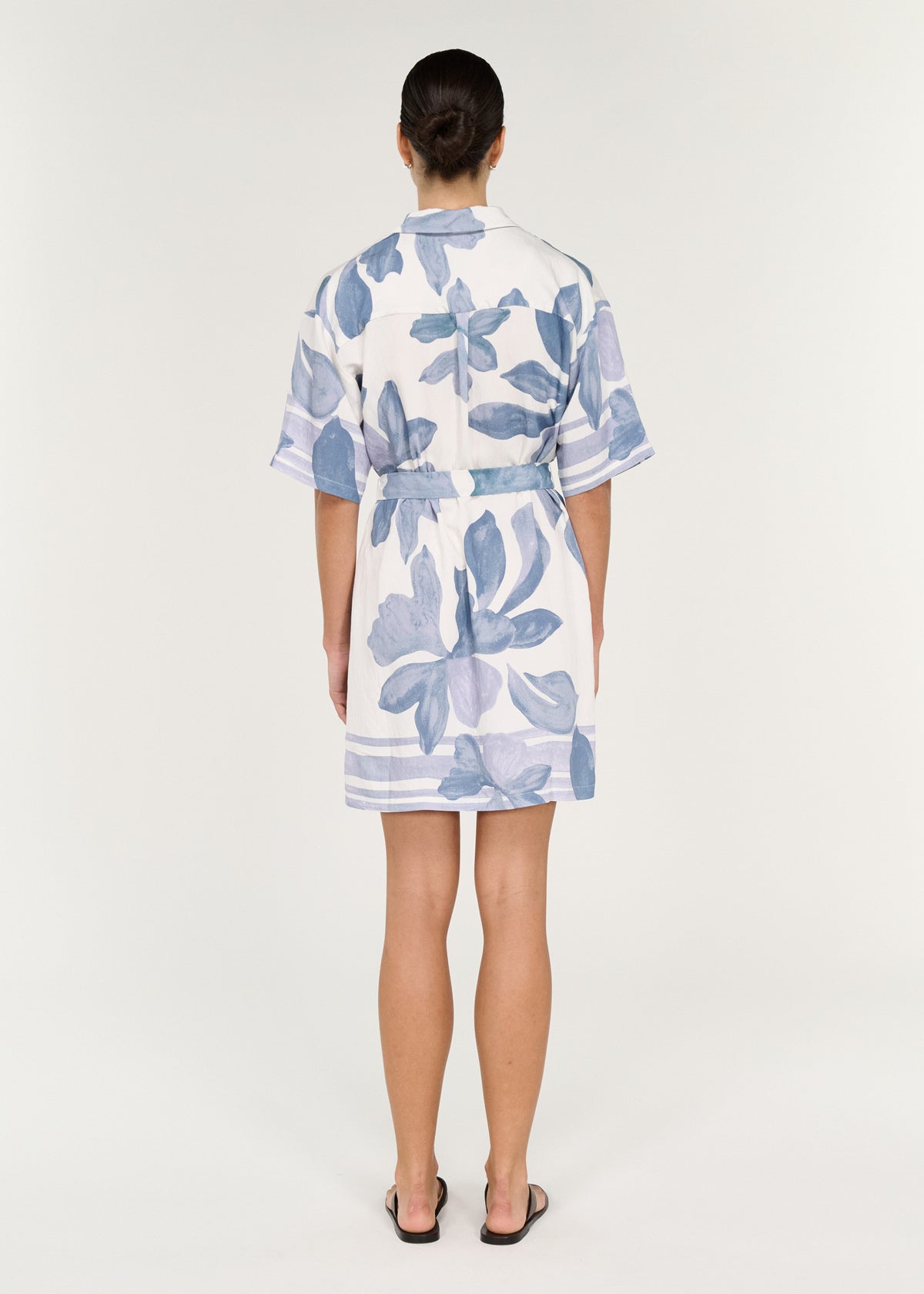 Back view of a model wearing a Mini Shirtdress in Blue Floral with oversized fit and self-tie waist belt.