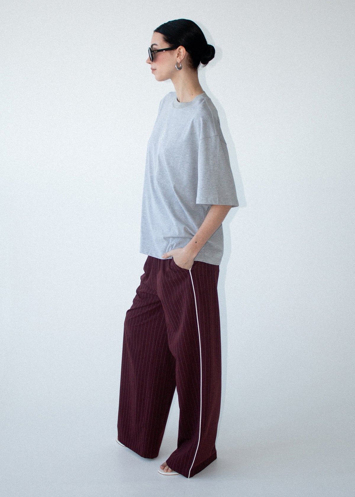 Model wearing Grey Marle Cotton Embroidered Oversized Tee with a subtle front logo detail, turned to the side.