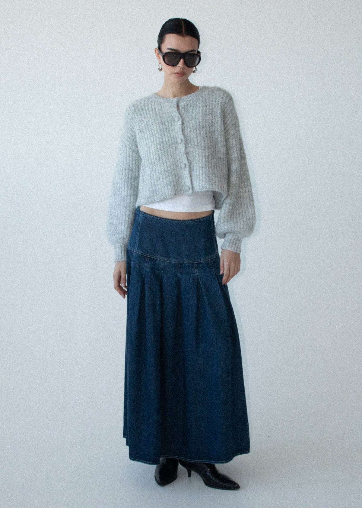 Model wearing Indigo Chambray Box Pleat Midi Skirt with a midi length and a back zip closure, photographed against a pale blue studio.