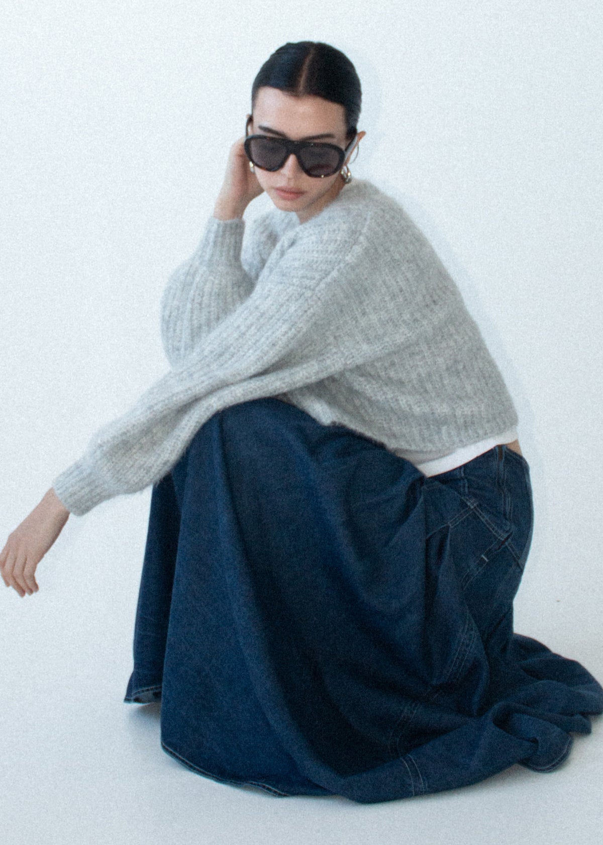 Model seated wearing Indigo Chambray Box Pleat Midi Skirt with a mid-weight denim fabrication and a fitted high waist.