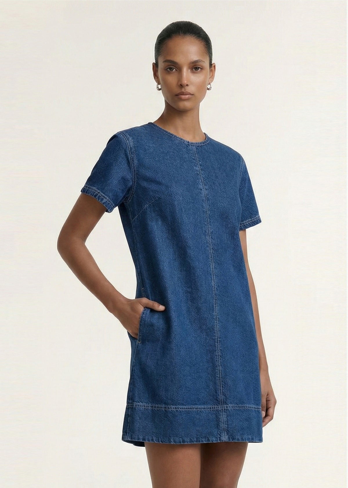 Model wearing Indigo Chambray Short Sleeve Mini Dress with a mid-weight denim fabrication and a round neckline.