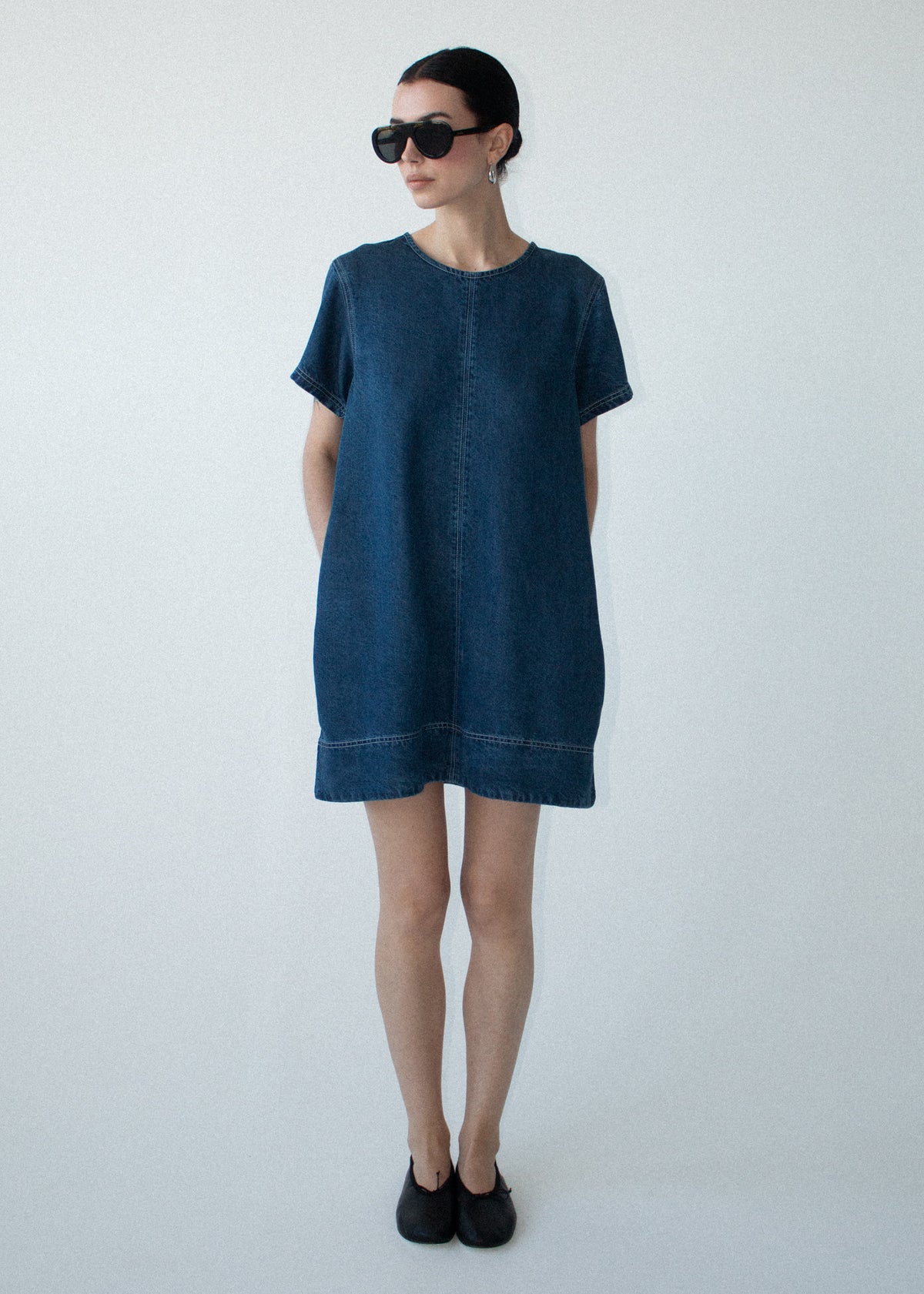 Model wearing Indigo Chambray Short Sleeve Mini Dress, showing short sleeves and a paneled seam detail.