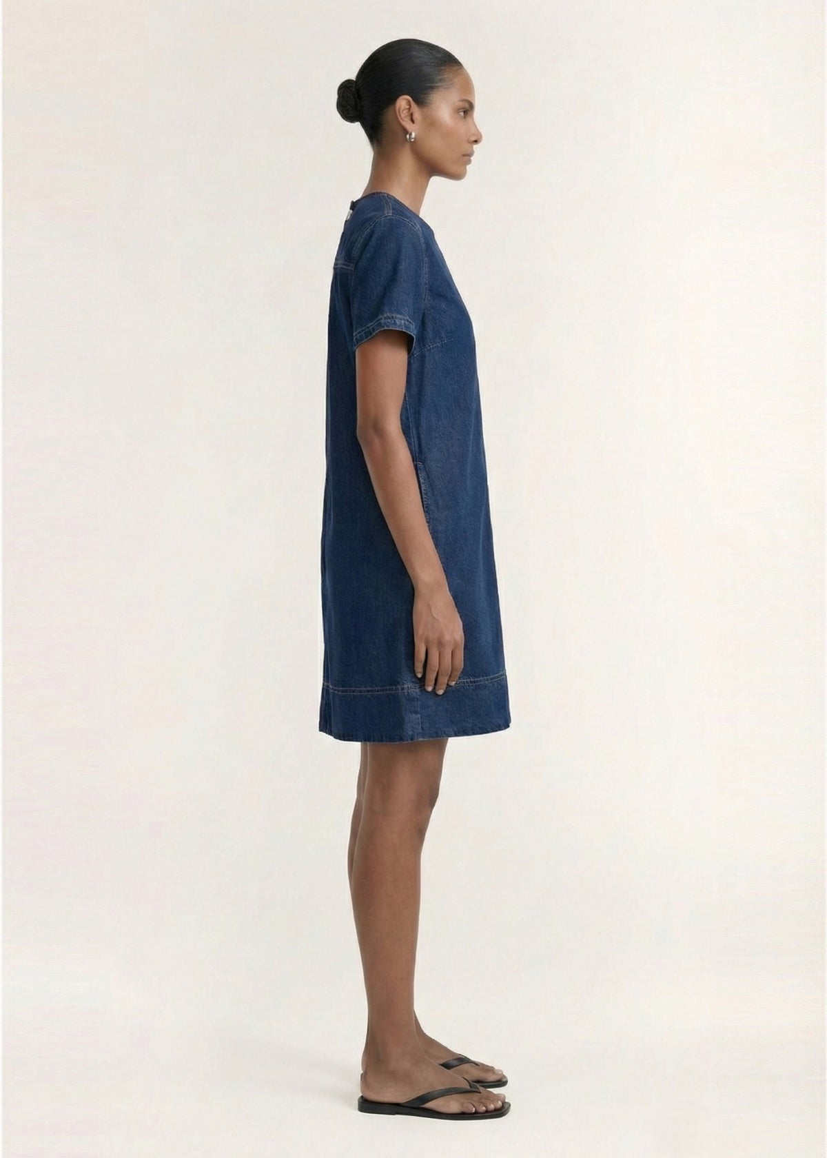 Side profile of the Indigo Chambray Short Sleeve Mini Dress with a paneled seam detail and a shift silhouette.