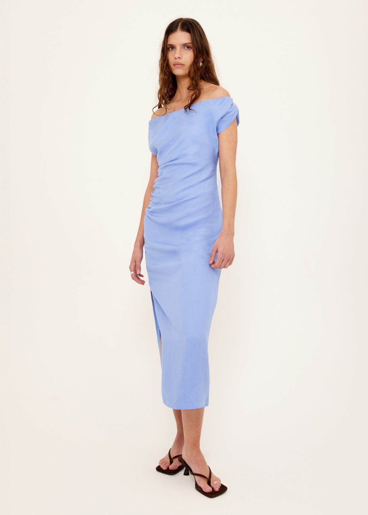 Model wearing Jacaranda Tencel Linen Blend Off-Shoulder Midi Dress with a side ruching and a side split, turned to the side.