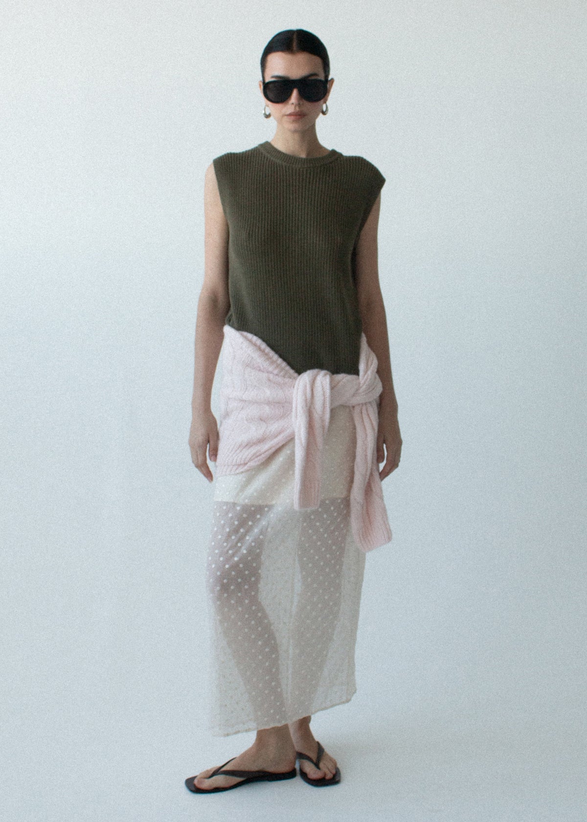 Model wearing Khaki Cotton Blend Knit Tank Top, showing a relaxed fit and a crew neckline, photographed against a pale blue studio.