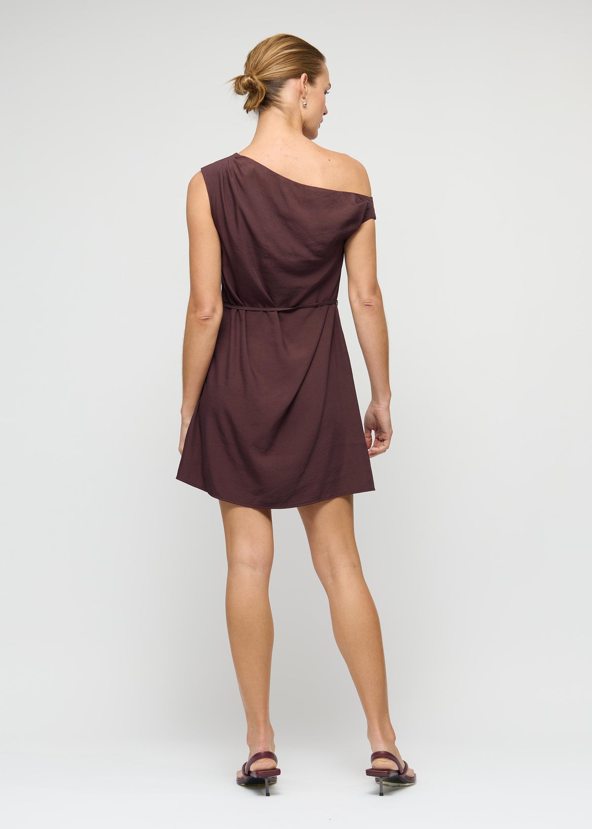 Back view of the Linen Blend Chocolate Asymmetrical Mini Dress with a statement self-tie bow detail and a one-shoulder neckline.