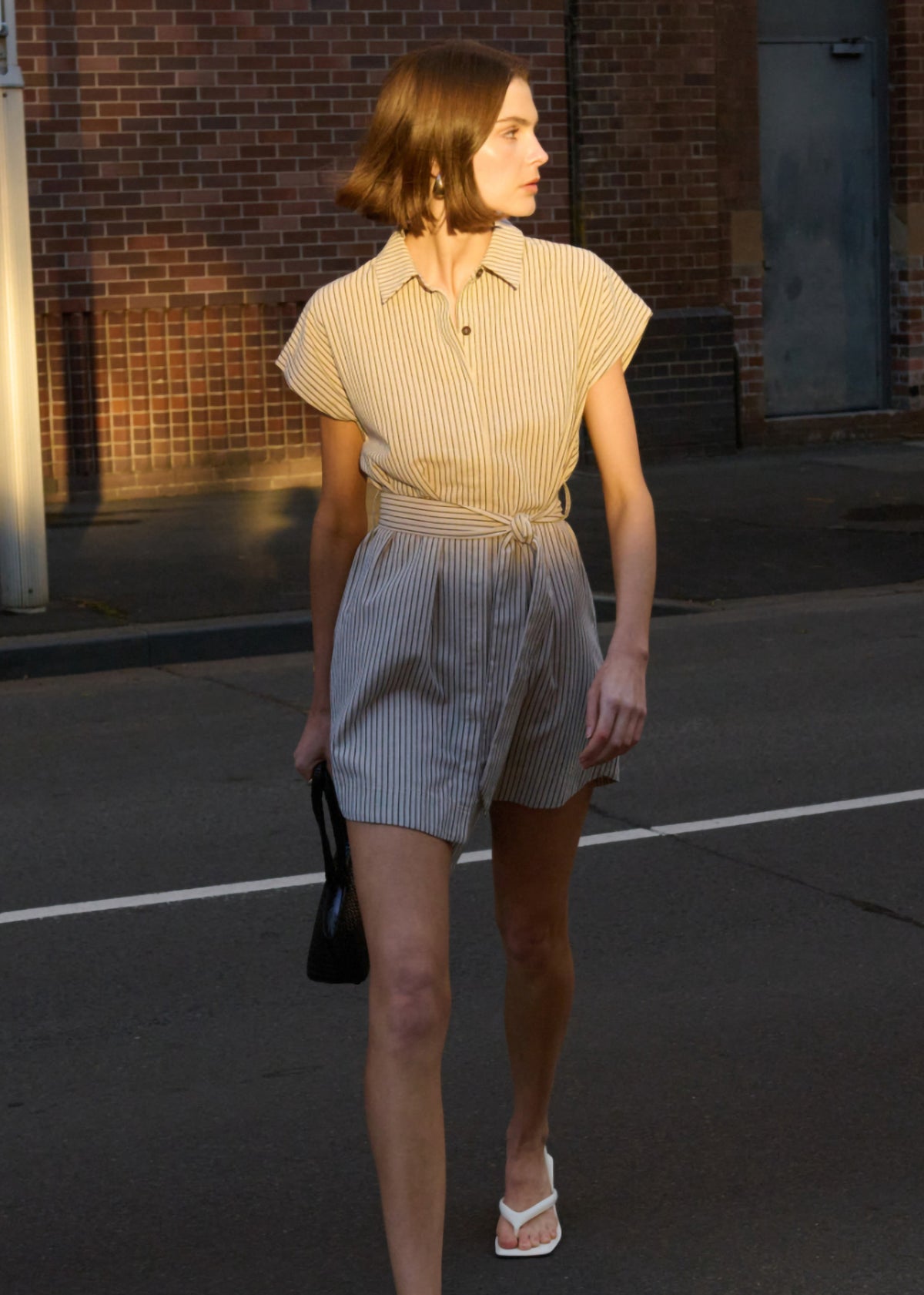 Model wearing Linen Blend Pinstripe Mini Shirt Dress with an adjustable self-tie waist and cap sleeves, turned to the side.