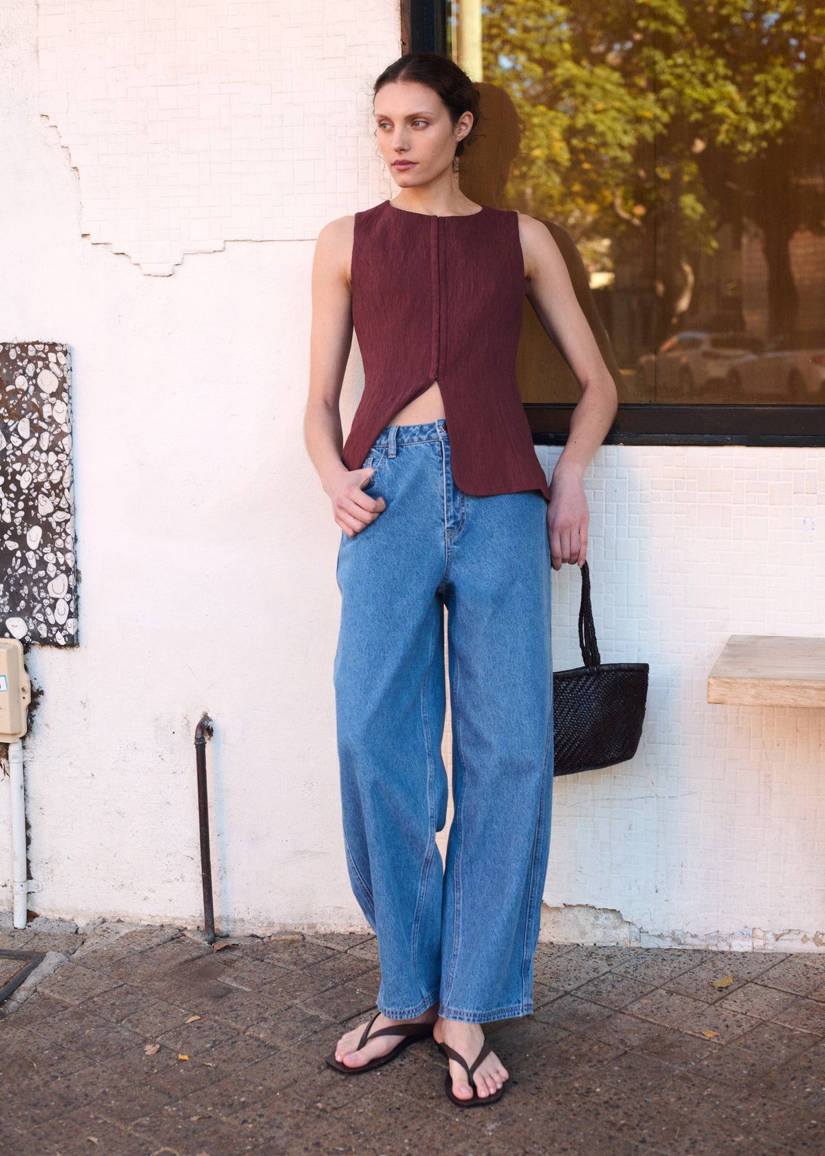 Model wearing Mid Blue Barrel Leg Denim Jeans, showing a high-rise fit and a full length design, photographed against a white wall outdoors.