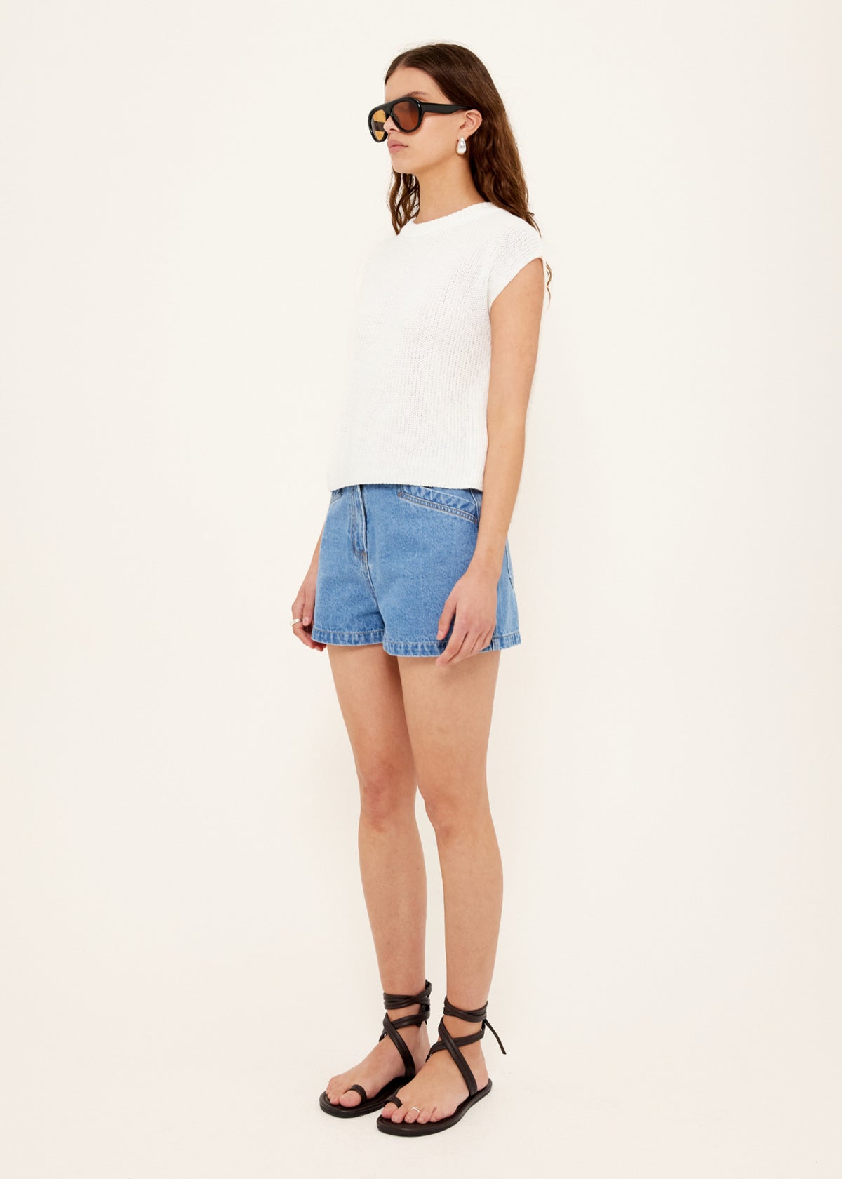 Model wearing Mid-Blue Denim Shorts with a classic light blue wash and a 100% Cotton denim, turned to the side.