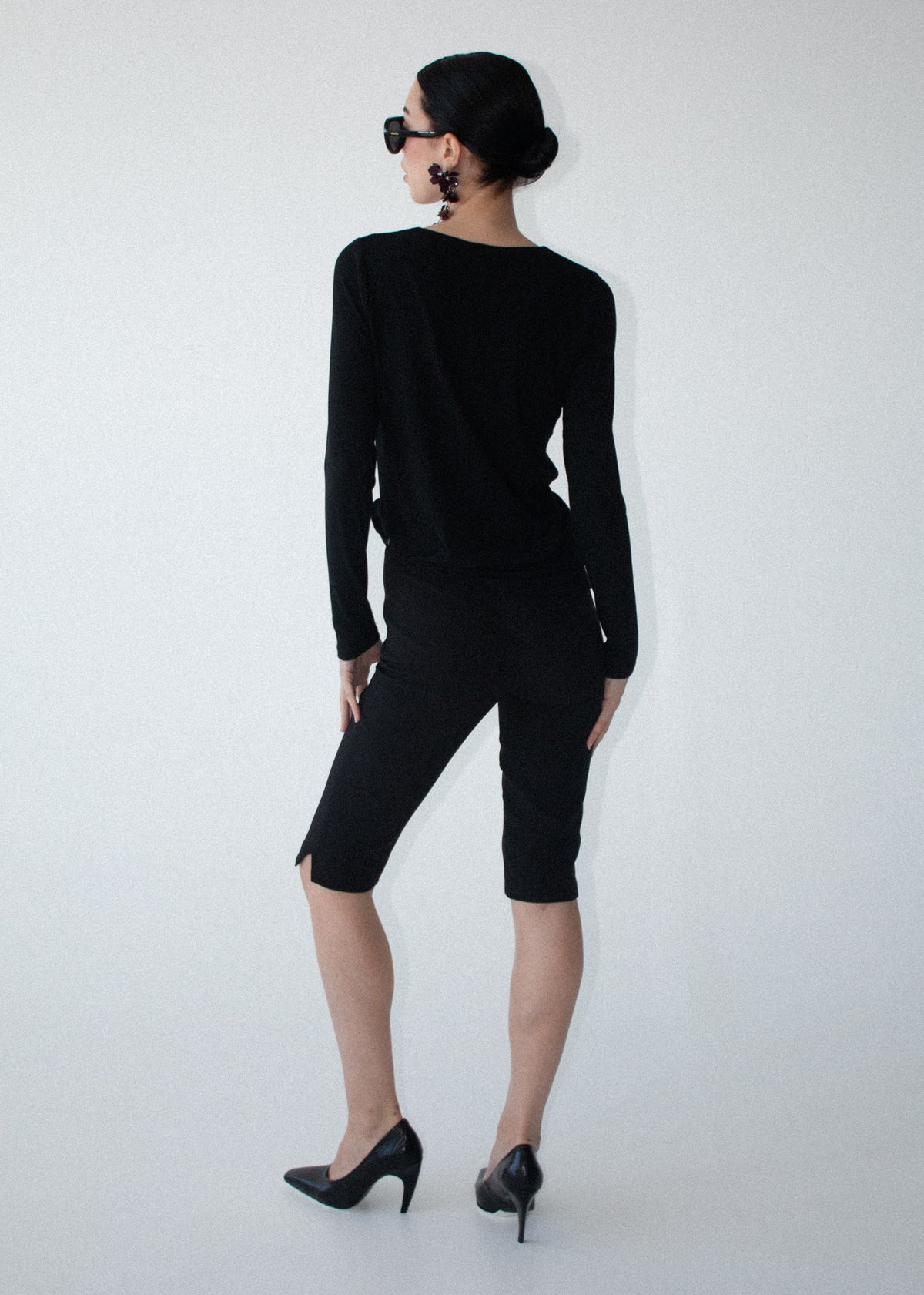 Model wearing Mid Rise Capri Pants in Black with a side zip closure and a subtle side splits at hem, photographed against a grey studio.