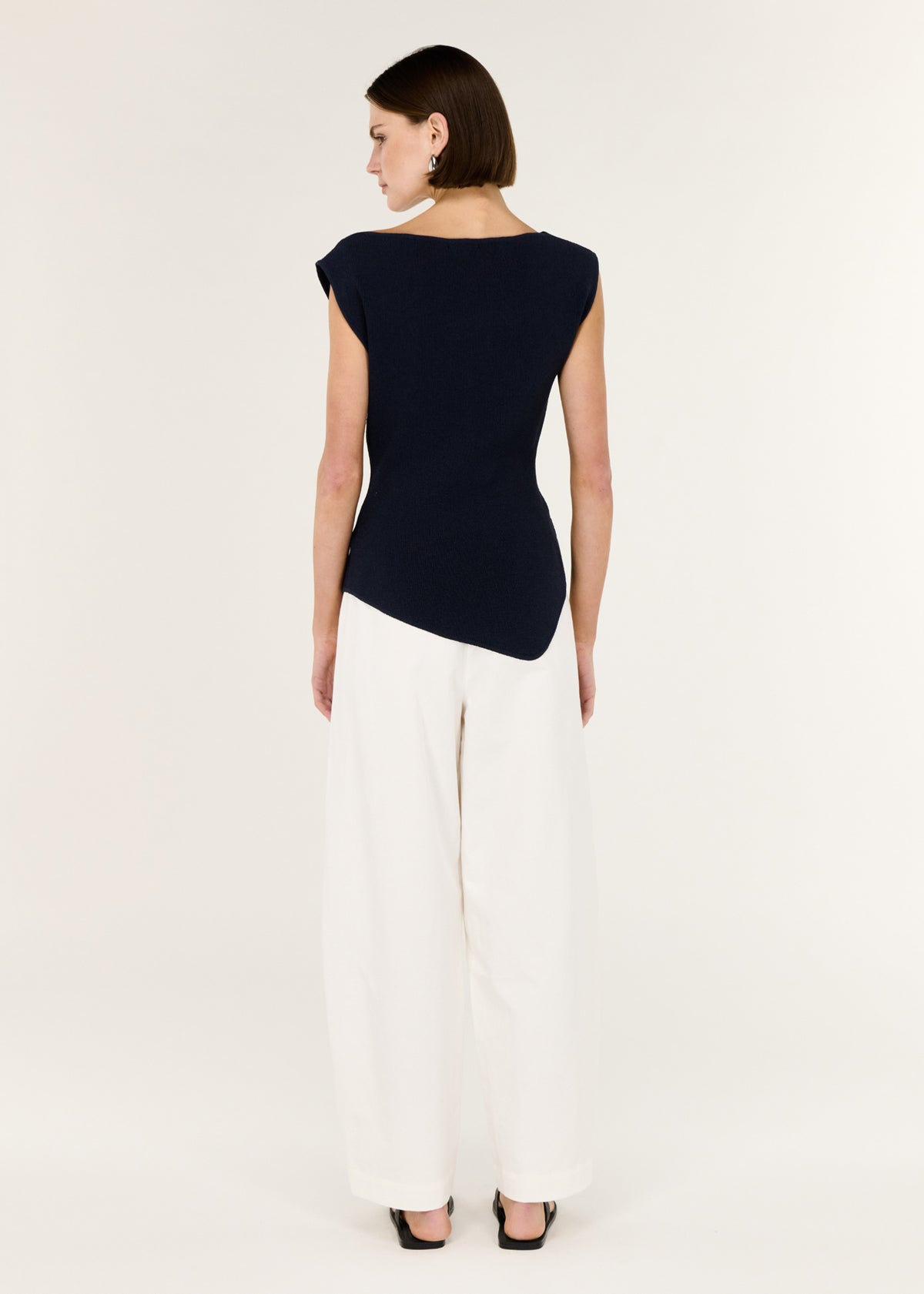 Back view of the Navy Boat Neck Knit Top with an asymmetrical hemline and a sleeveless cut.