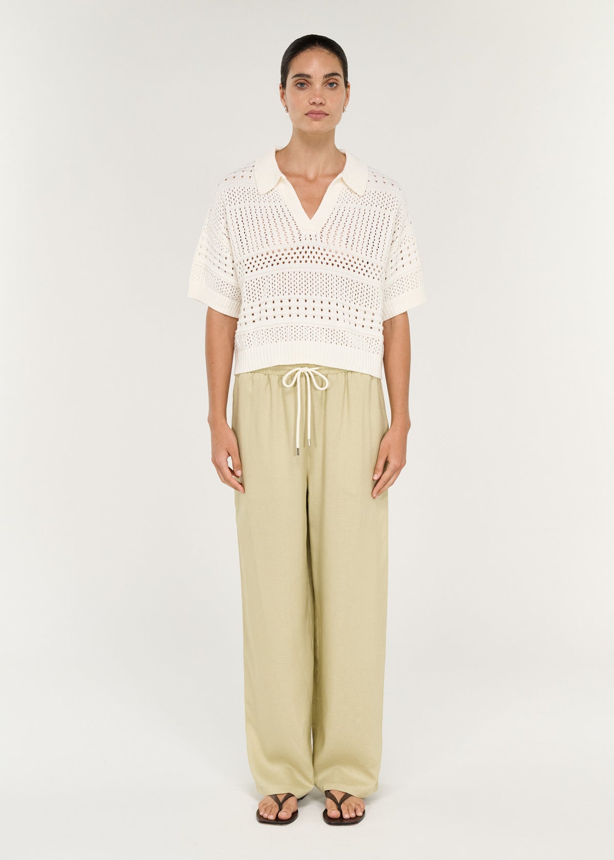 Model wearing a Relaxed Crochet Polo Shirt in Cream with wide beige pants, showcasing a V-neck and short sleeves.