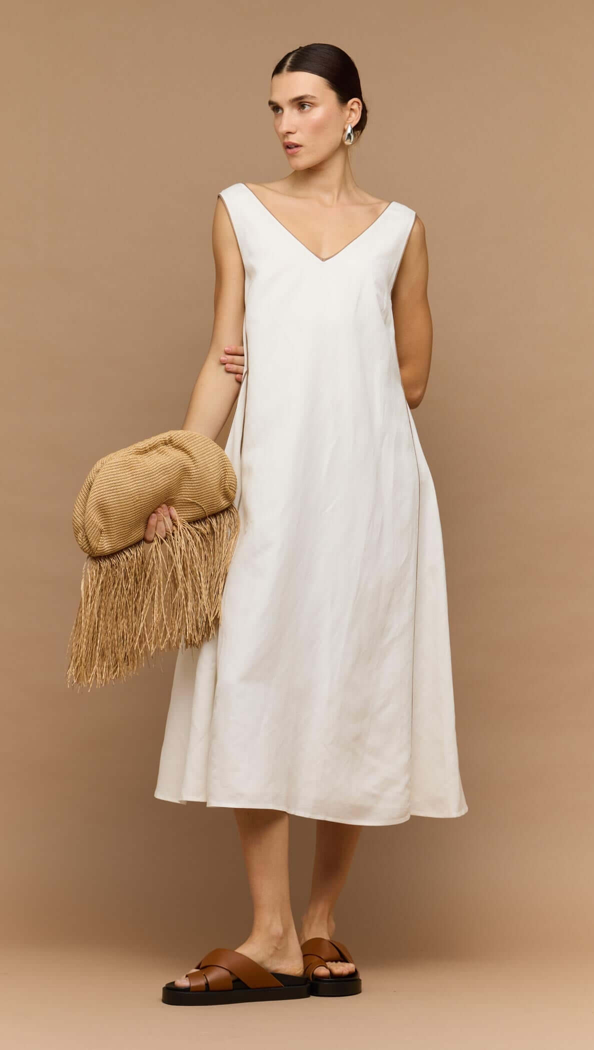 Model wearing a White Godet Linen Midi Dress, featuring a V-neckline and a softly flared skirt, paired with a stylish clutch.