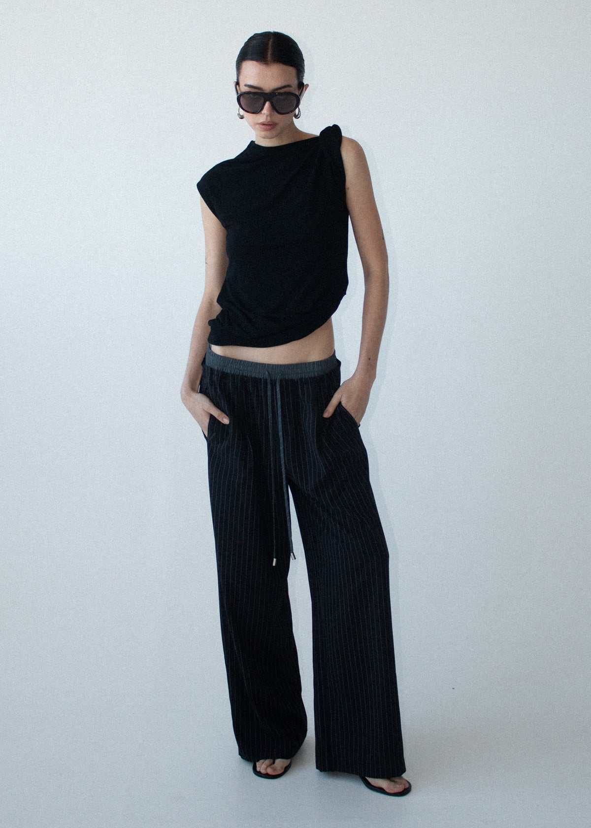 Model wearing Pinstripe Relaxed Drawstring Pants with an adjustable drawcord tie and side seam pockets, turned to the side.