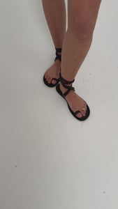 Feet wearing stylish black strappy sandals on a white background.