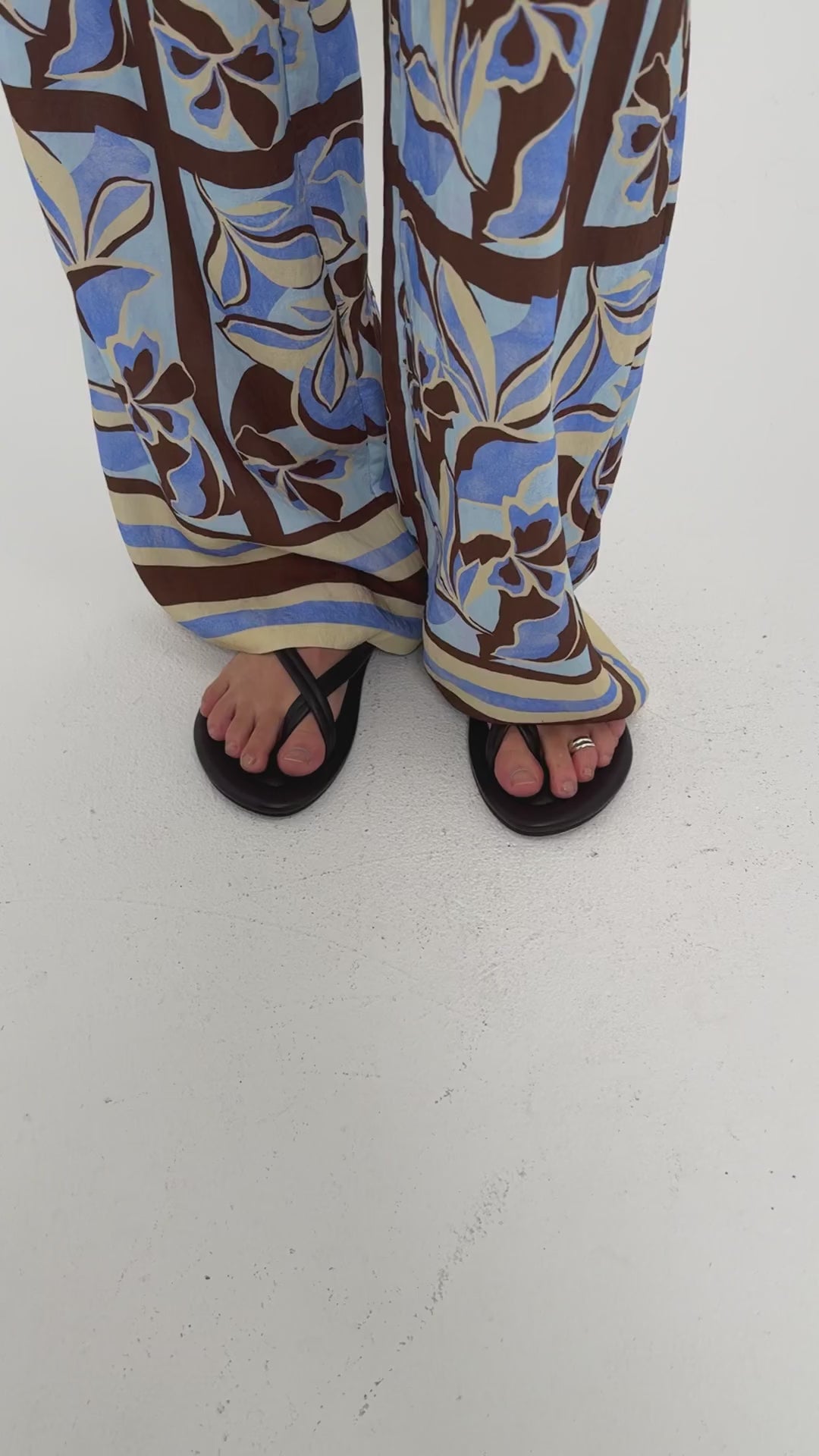 Model wearing patterned pants with blue and brown floral design and black flip-flops, showcasing a casual summer look.
