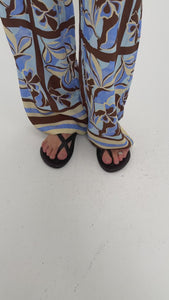 Model wearing patterned pants with blue and brown floral design and black flip-flops, showcasing a casual summer look.