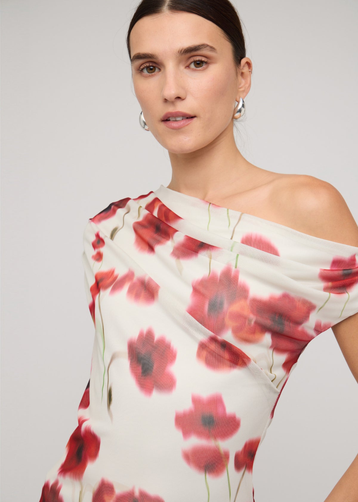 Close-up of Red and White Poppy Print Off-Shoulder Mesh Top with a one-shoulder draped neckline and a blurred floral print.