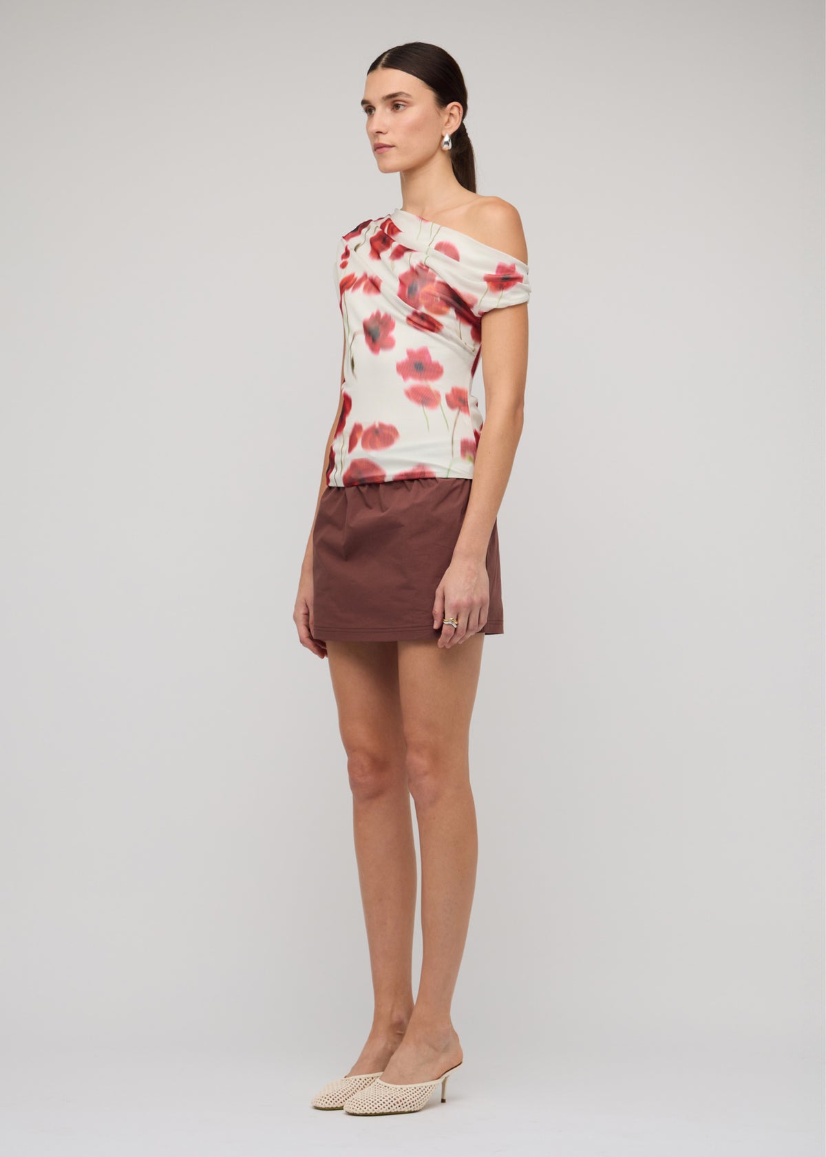 Model wearing Red and White Poppy Print Off-Shoulder Mesh Top with a one-shoulder draped neckline, turned to the side.