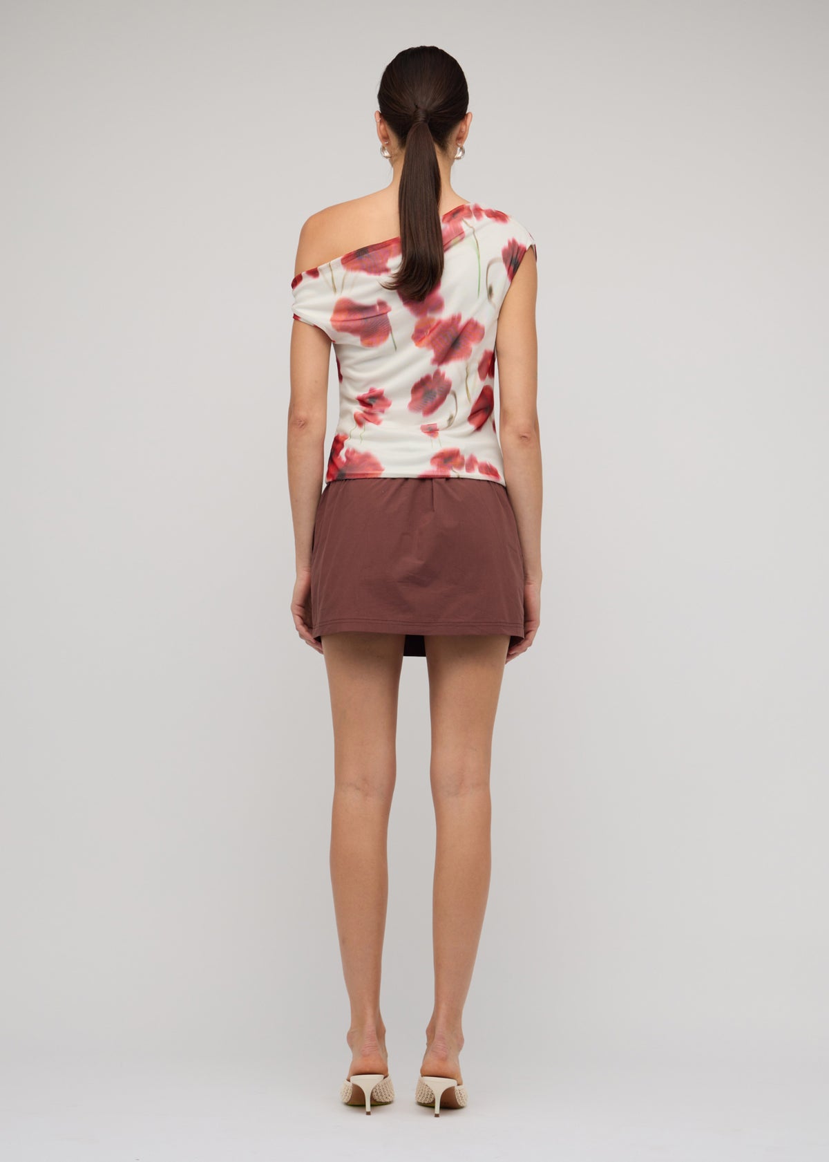 Back view of the Red and White Poppy Print Off-Shoulder Mesh Top with a one-shoulder draped neckline and a blurred floral print.