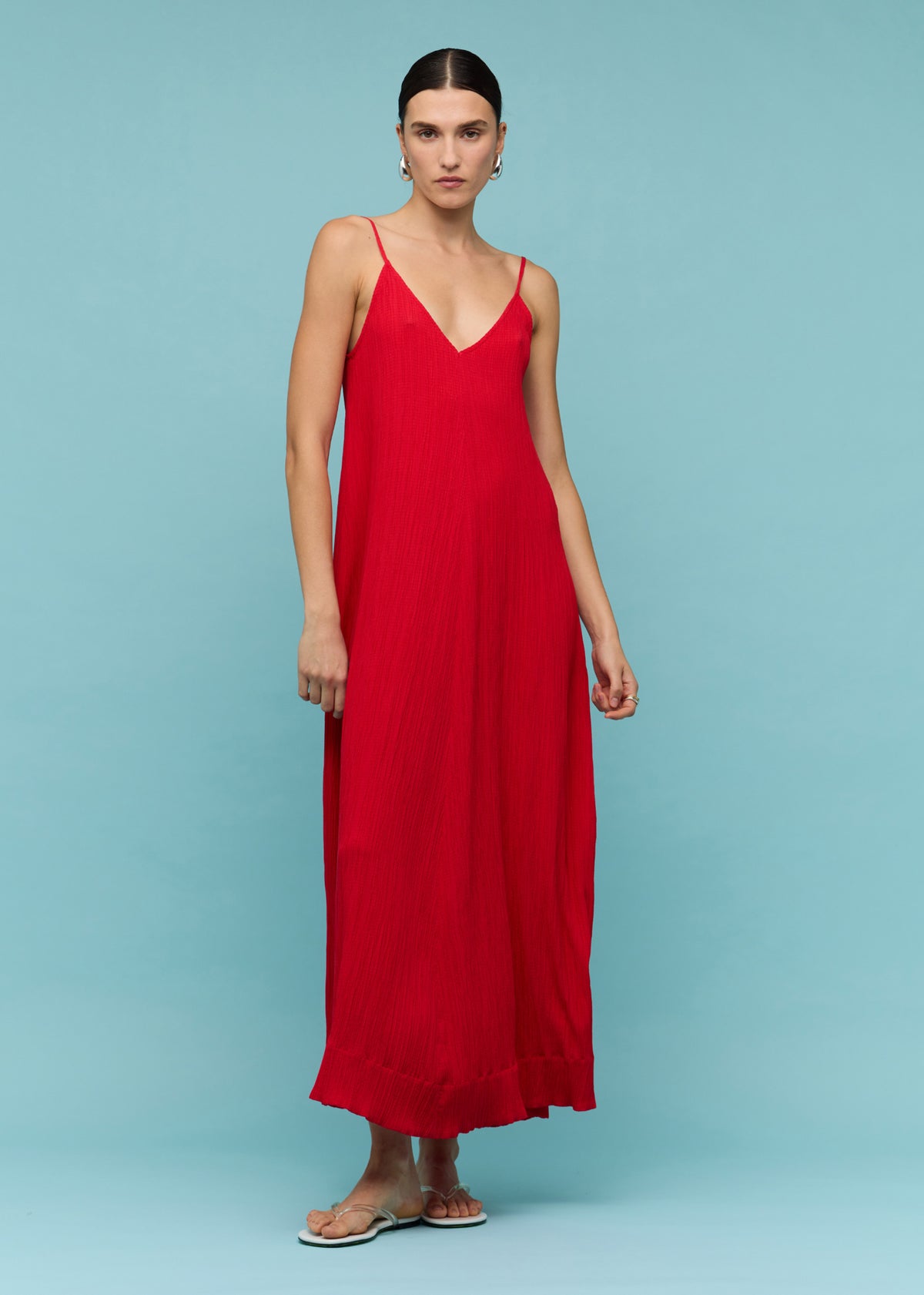 Model wearing Red Crepe V-Neck Floaty Maxi Dress, showing slim adjustable straps, photographed against a turquoise blue backdrop.