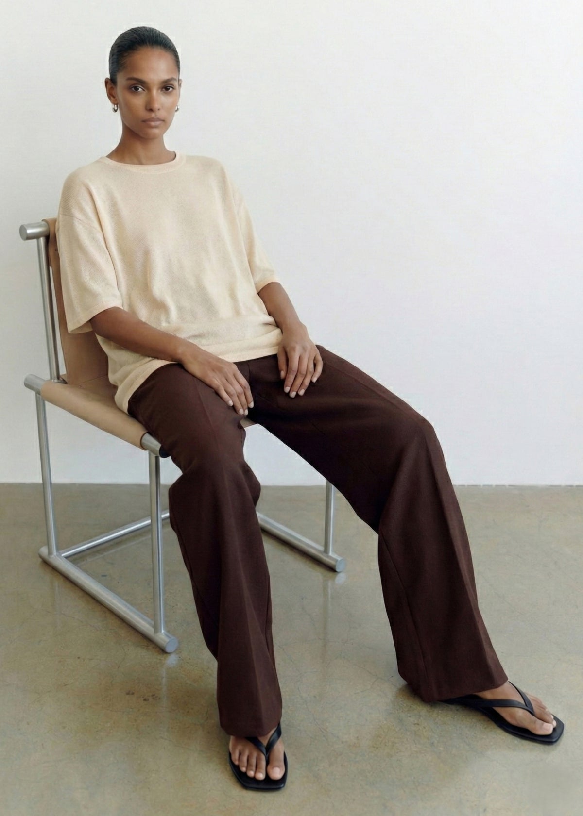 Model seated wearing Round Neck Oversized Knit Tee in Ecru with dropped shoulders and elbow-length sleeves.