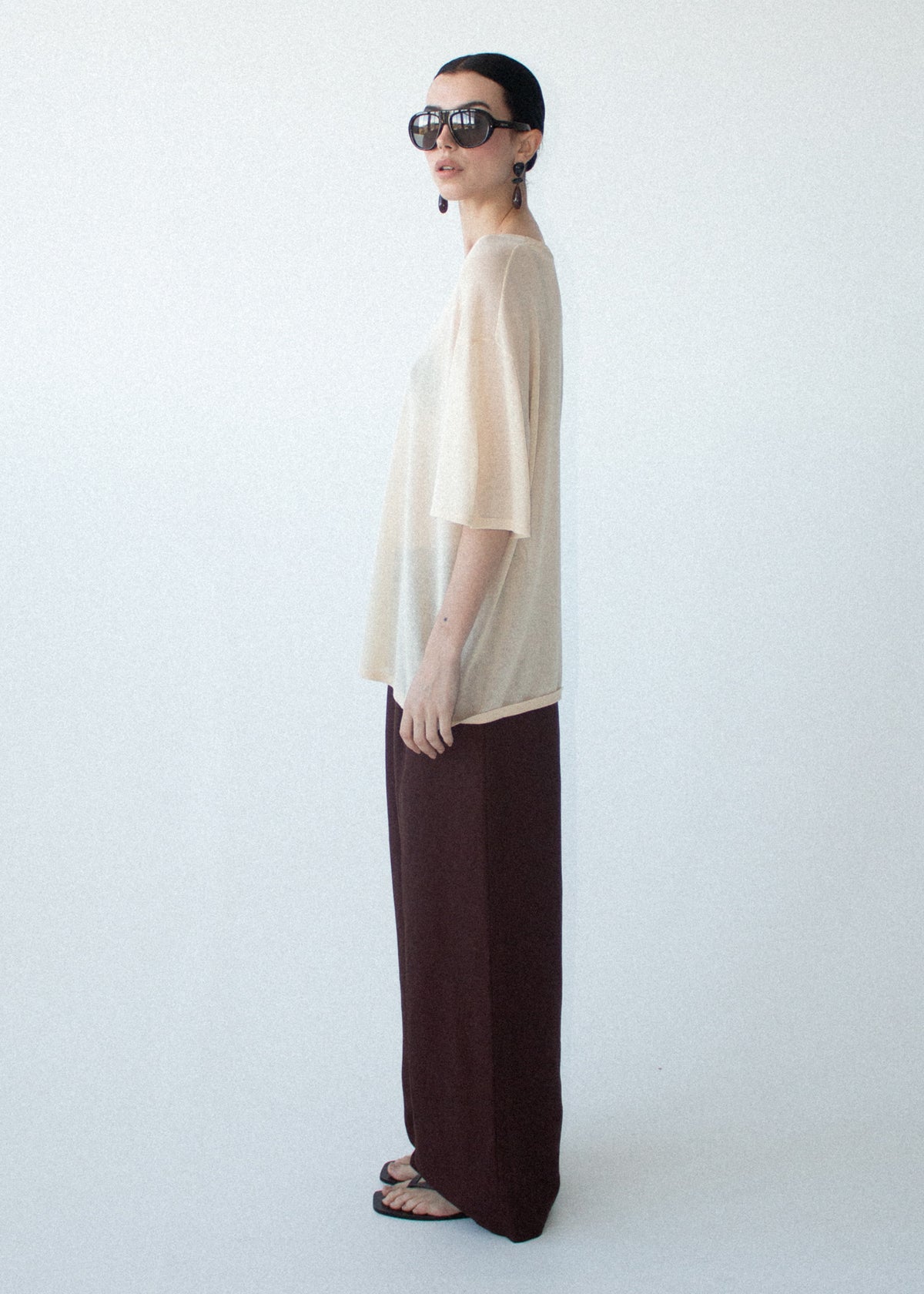 Model wearing Round Neck Oversized Knit Tee in Ecru with an oversized silhouette and a relaxed fit, turned to the side.