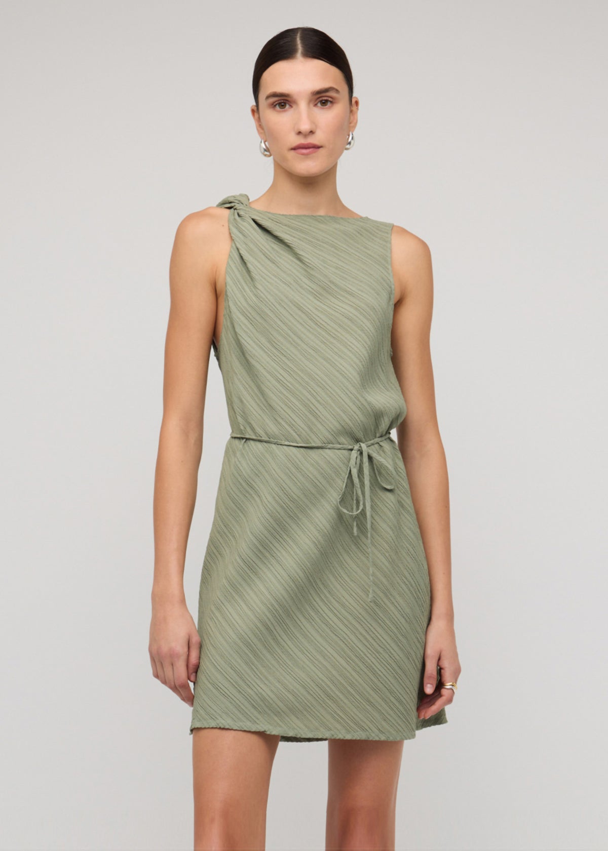 Model wearing Sage Green Mini Dress With Tie Waist with a textured fabrication and a sleeveless cut.