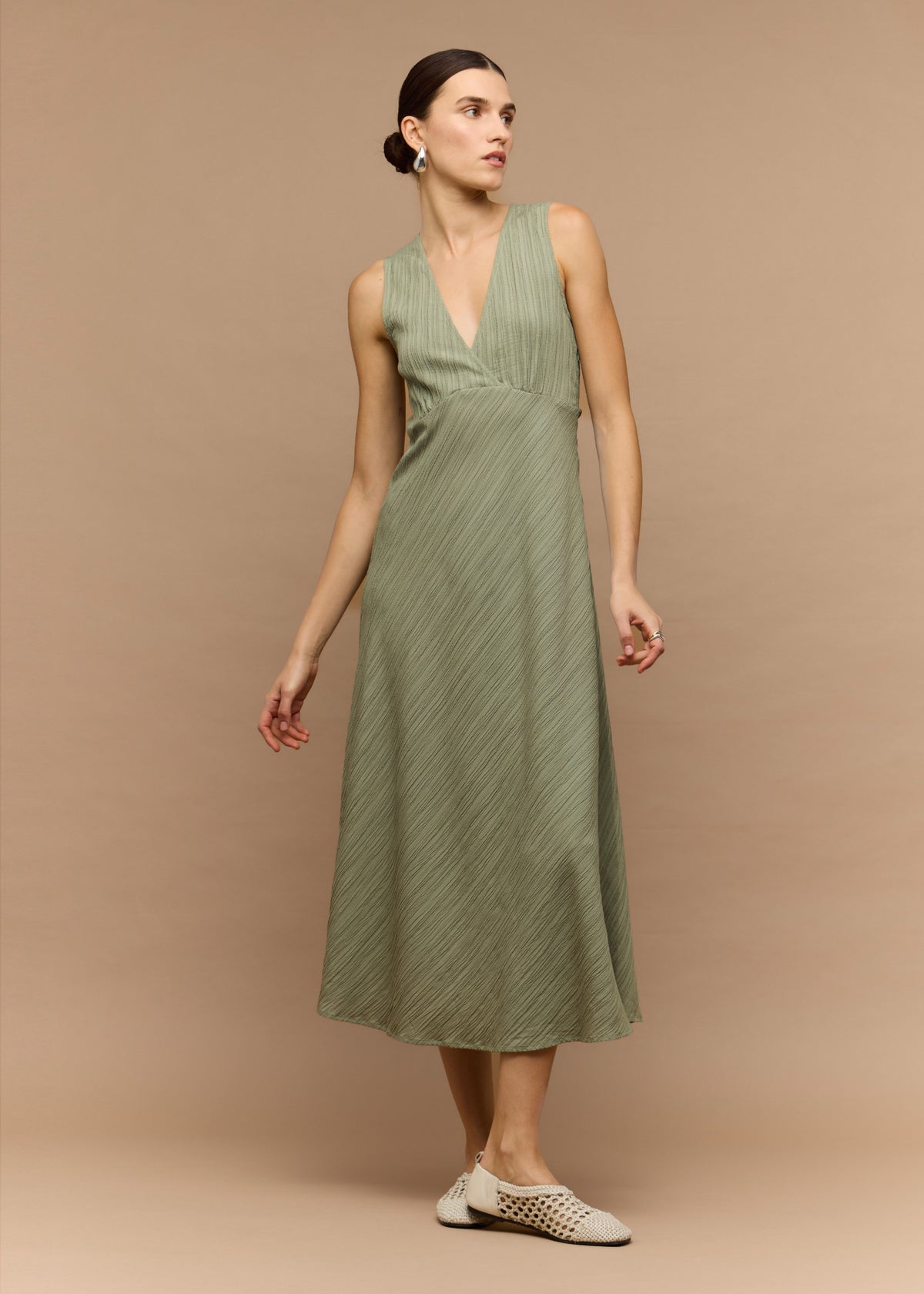 Model wearing Sage Green V-Neck Bias Midi Dress, showing an adjustable waist tie at the back and a midi length.