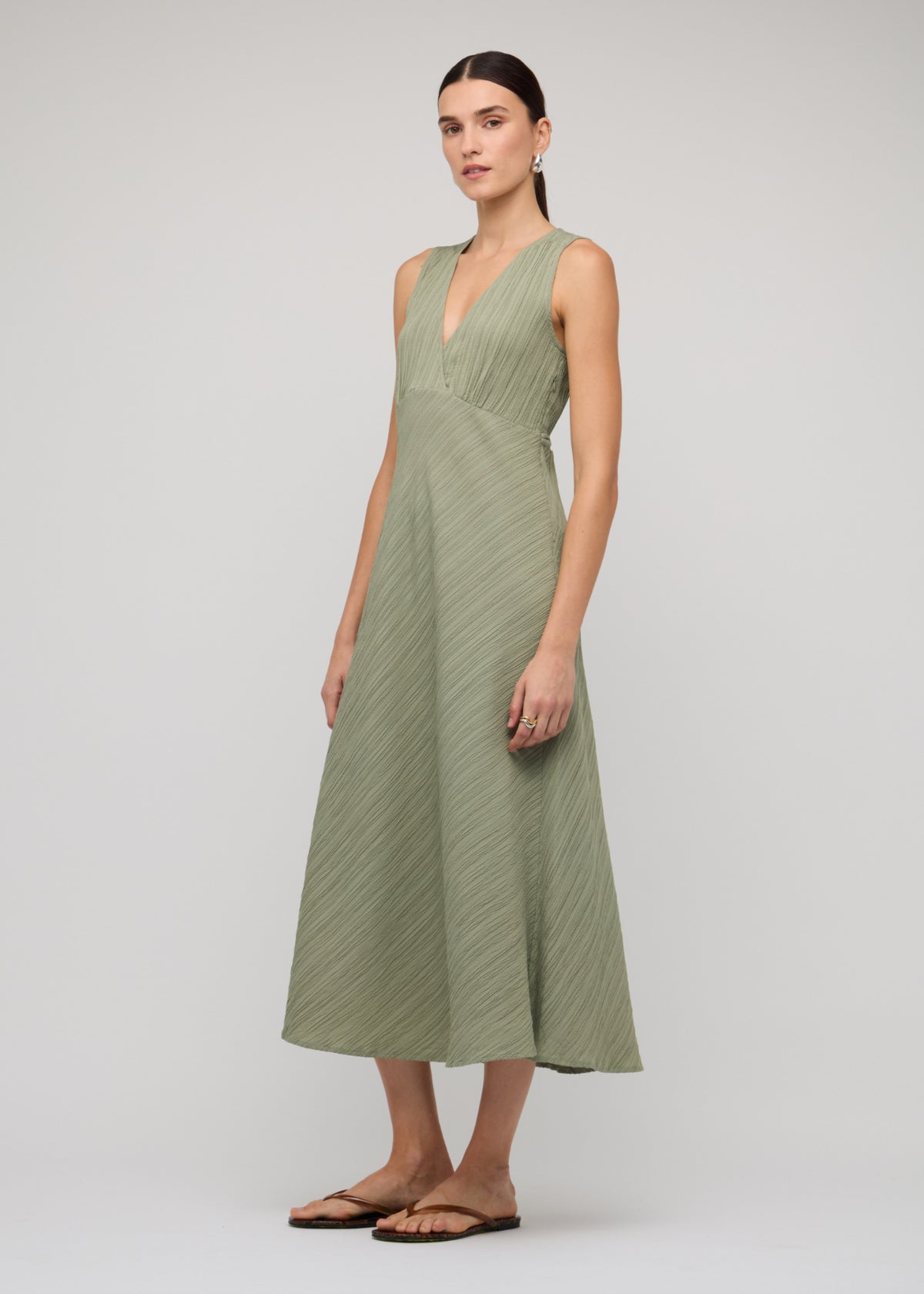 Angled view of the Sage Green V-Neck Bias Midi Dress with a midi length and a sage green colour-way.