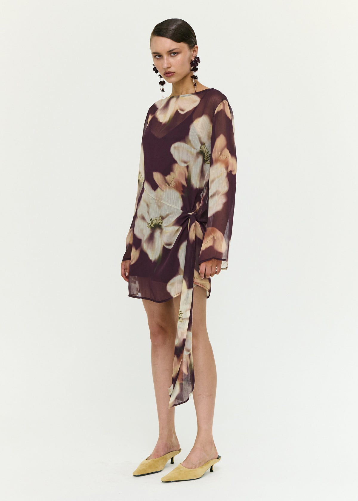 Model wearing Sheer Floral Mini Dress with Tie Detail with a polyester fabrication, turned to the side.