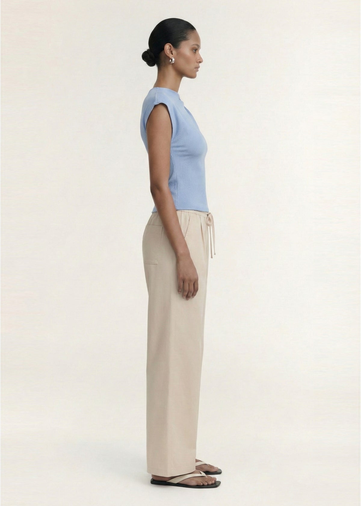 Model wearing Stone Cotton Wide Leg Drawstring Pant with a wide-leg silhouette and side pockets, turned to the side.