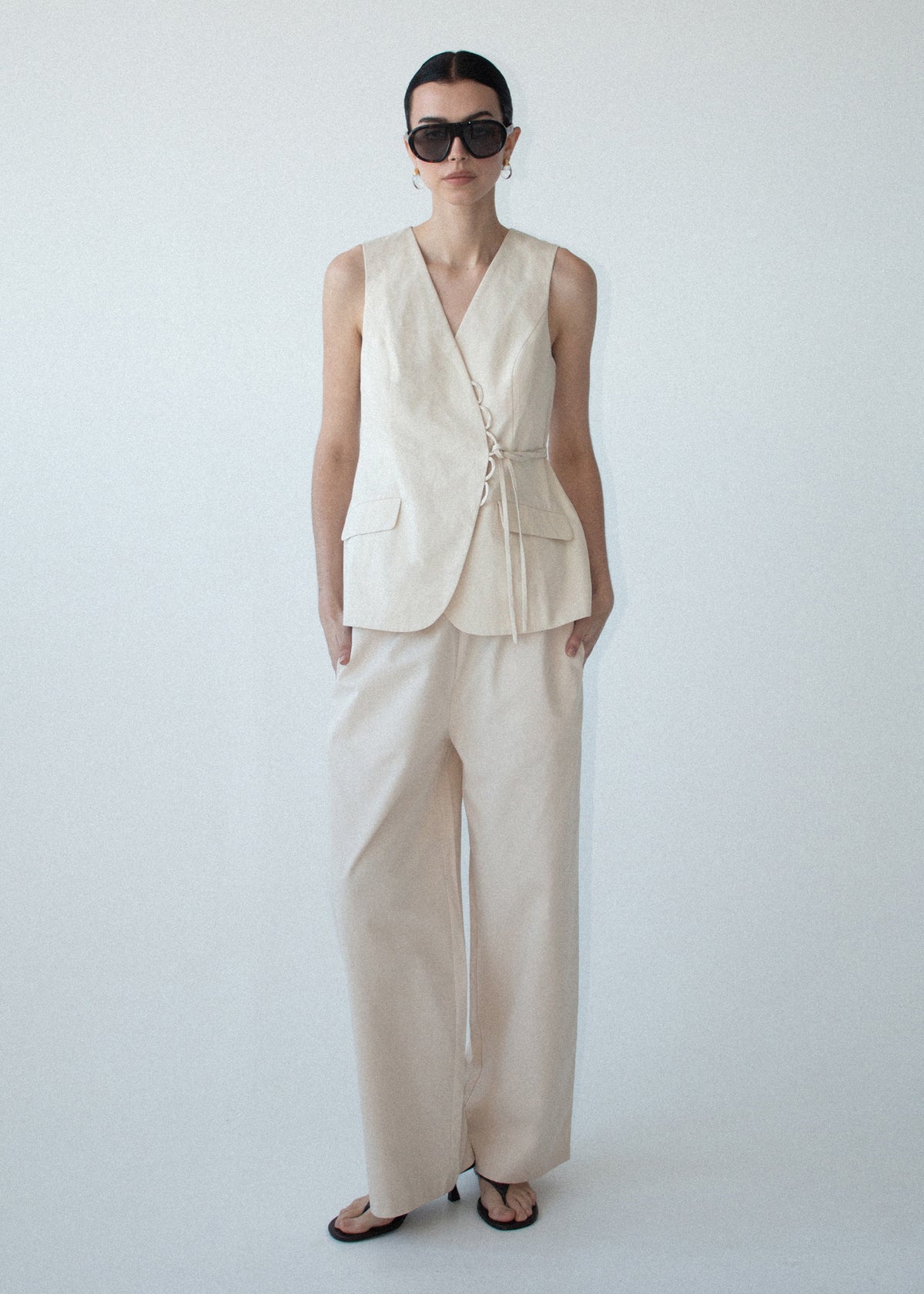 Model wearing Stone Cotton Wrap Front Vest with a sleeveless silhouette and a longline length.