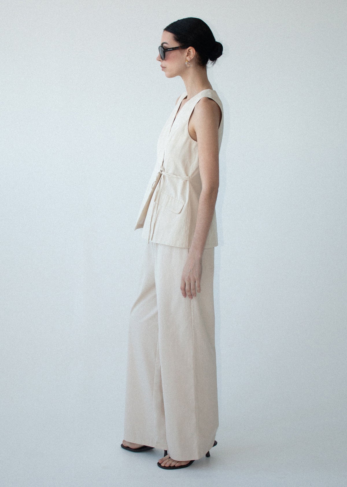 Model wearing Stone Cotton Wrap Front Vest with a lightweight structured fabrication and a wrap-front V-neckline, turned to the side.