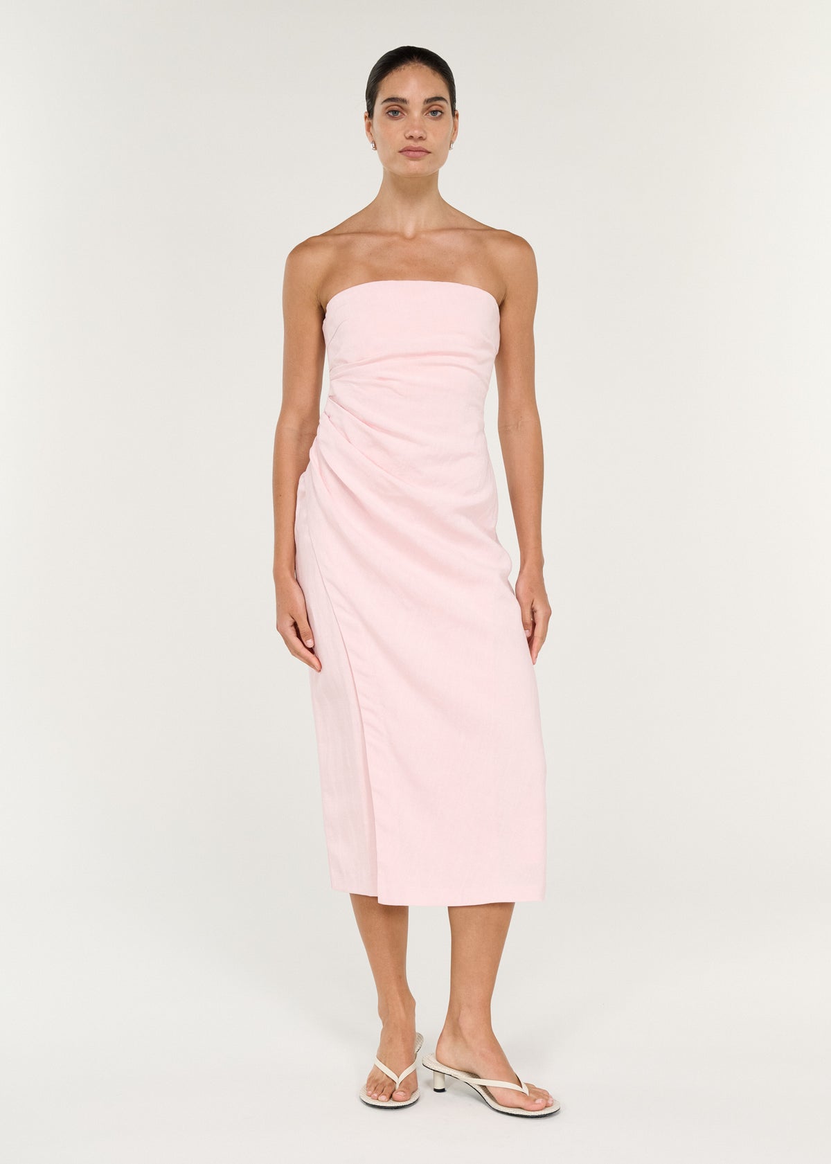 Model wearing Strapless Wrap Midi Dress in Soft Pink with a fitted bodice and a pleated side waist detailing.