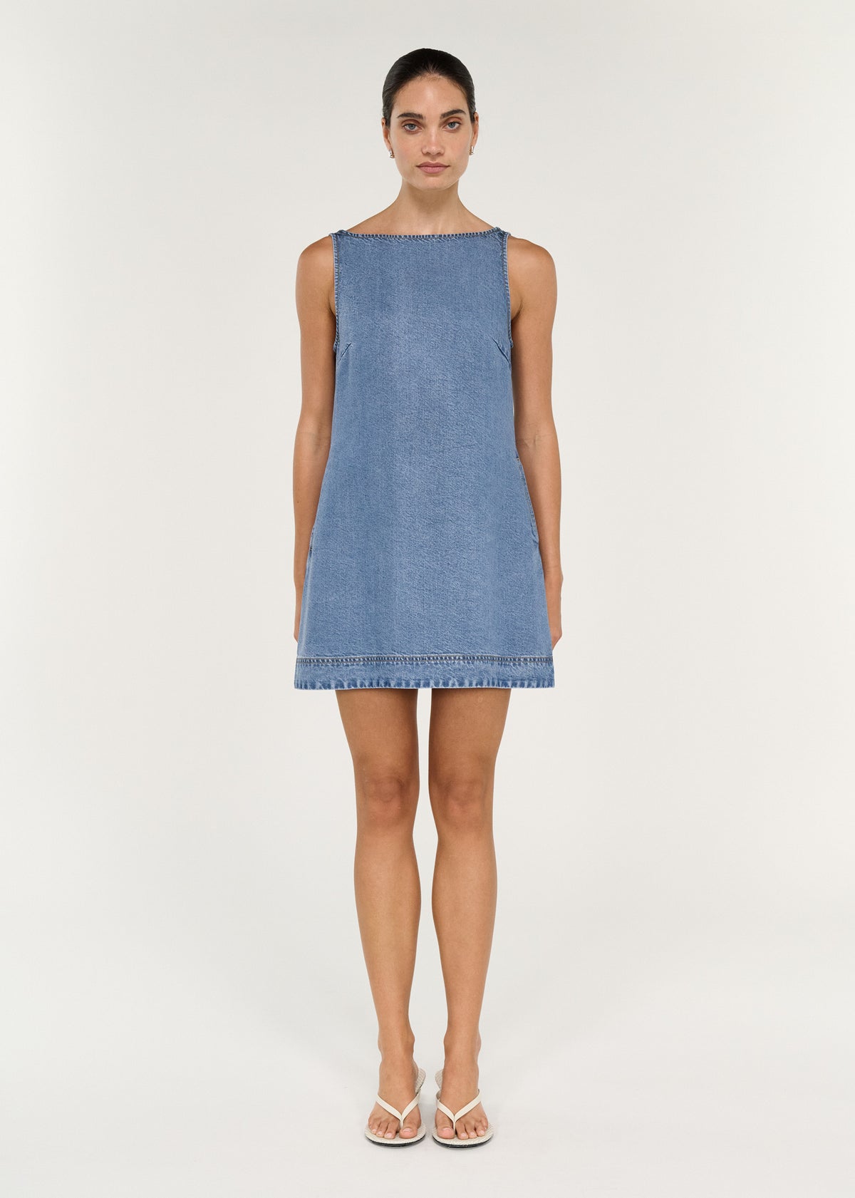Chambray Denim Sleeveless Mini Dress on model showcasing a relaxed A-line silhouette and high boat neckline.