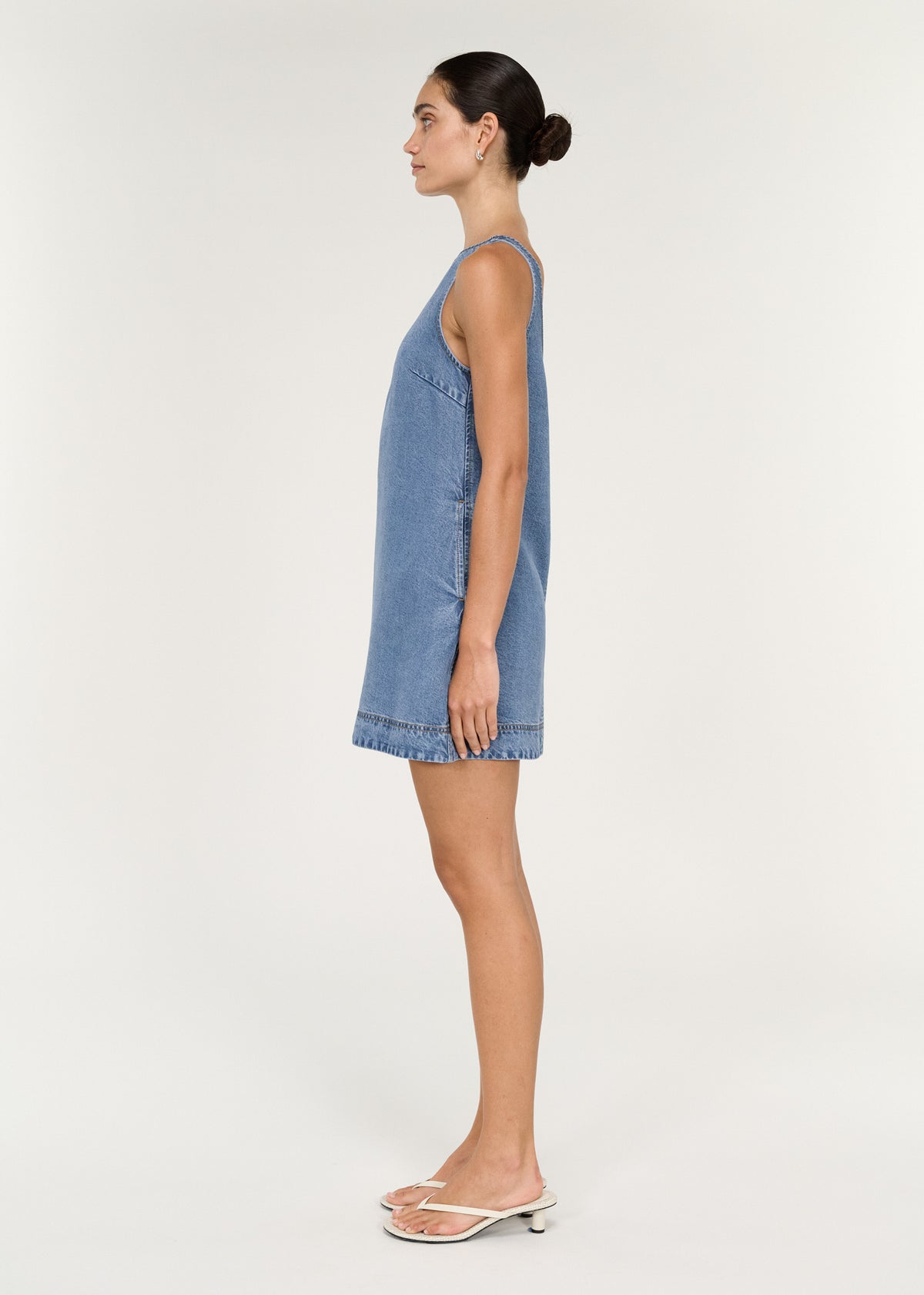 Chambray Denim Sleeveless Mini Dress side view model showcasing relaxed A-line silhouette and high boat neckline.