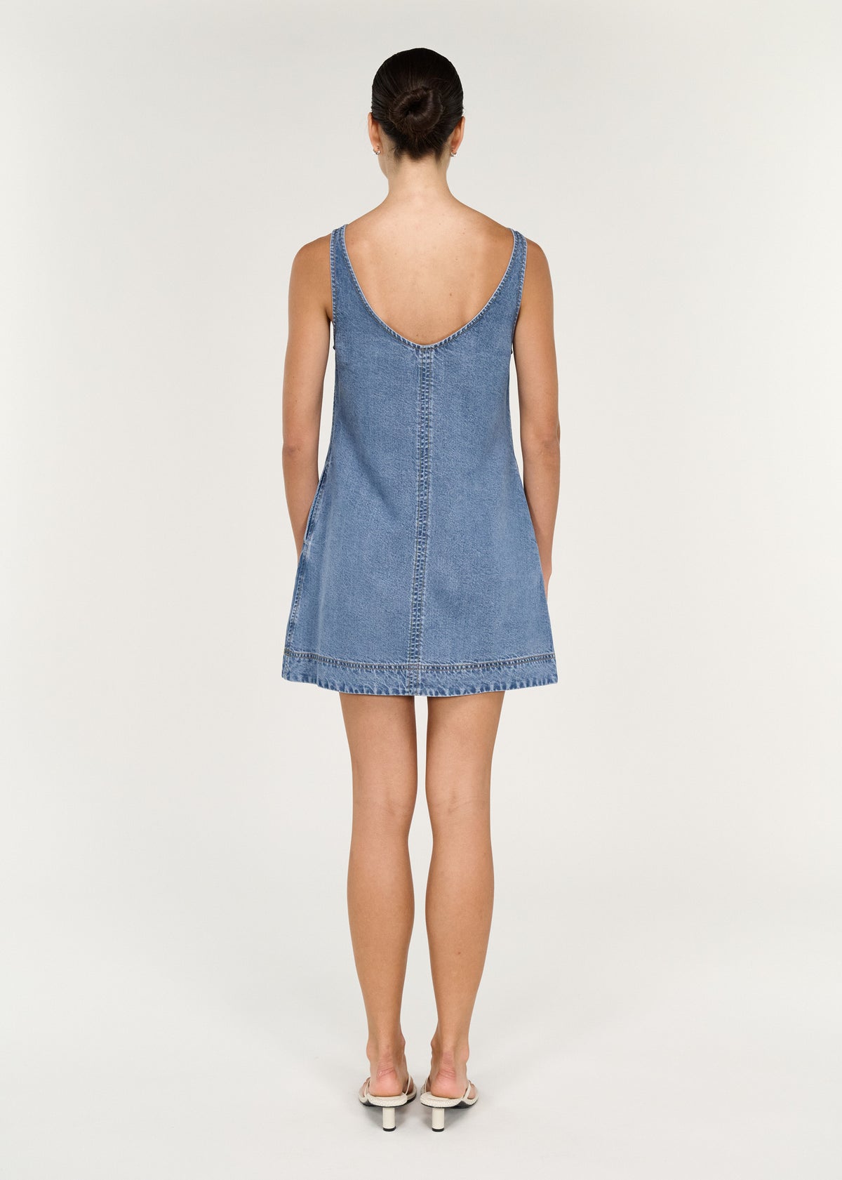 Back view of woman wearing Chambray Denim Sleeveless Mini Dress with a relaxed A-line silhouette and contrast stitching.